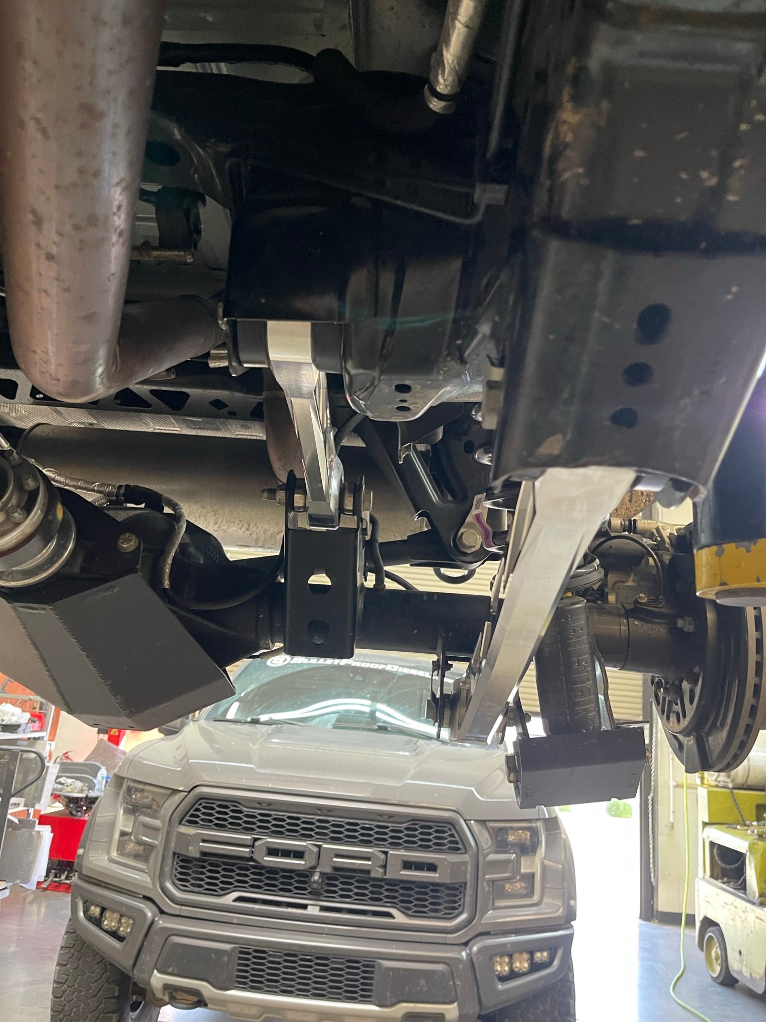 Bronco rear suspension kit featuring billet aluminum rear arms installed under a vehicle in a workshop setting.