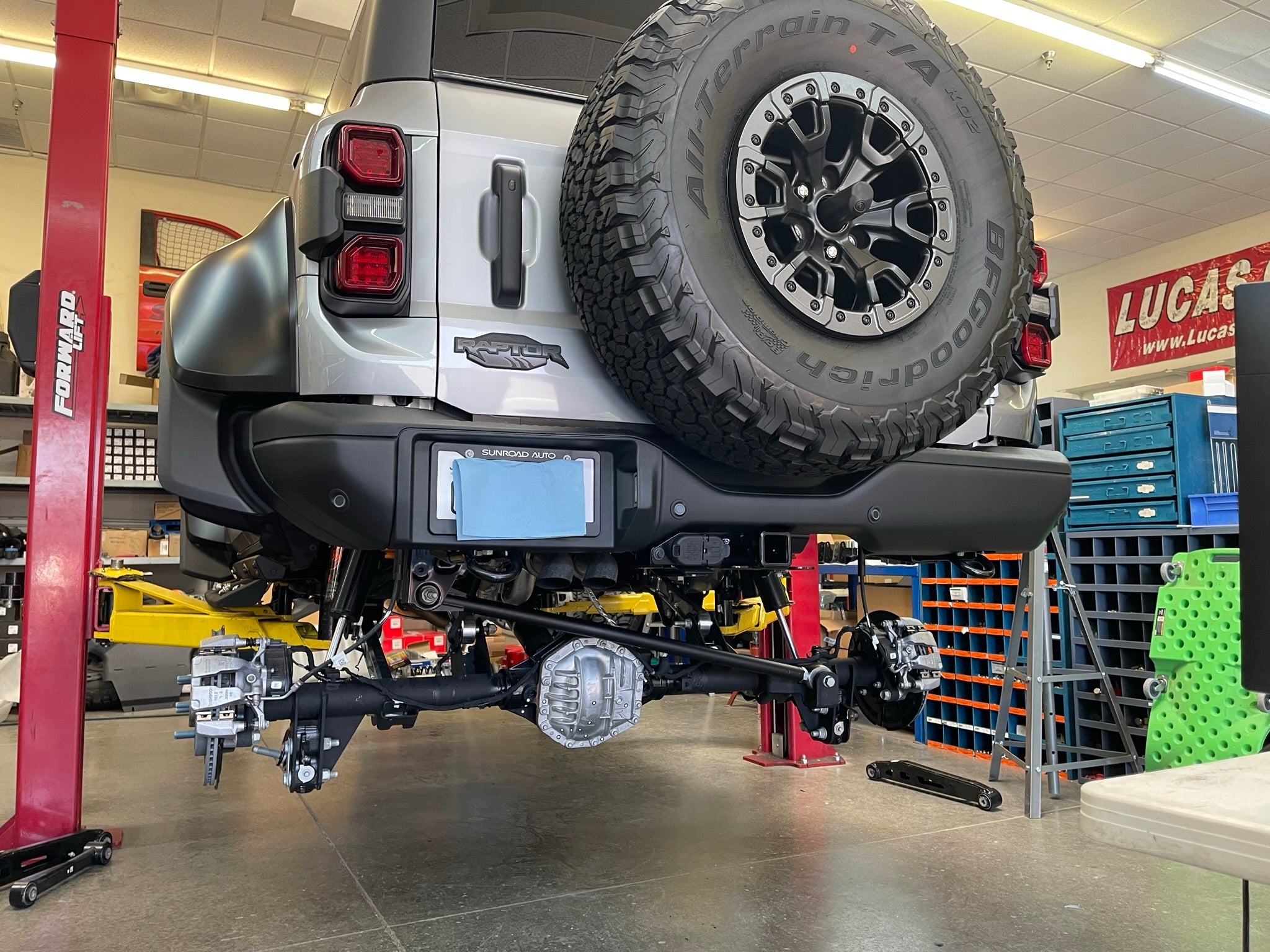 Bronco Raptor rear suspension kit featuring billet aluminum rear arms, displayed on a lifted vehicle in a workshop.