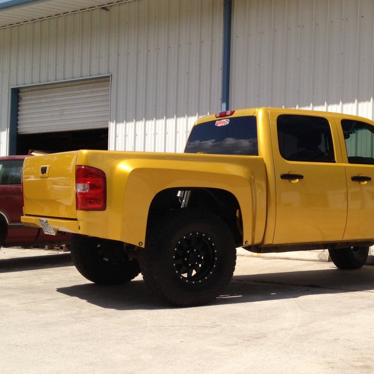 Yellow 2007-2013 Chevrolet Silverado showcasing custom bedsides and offroad tires, parked outside a garage.