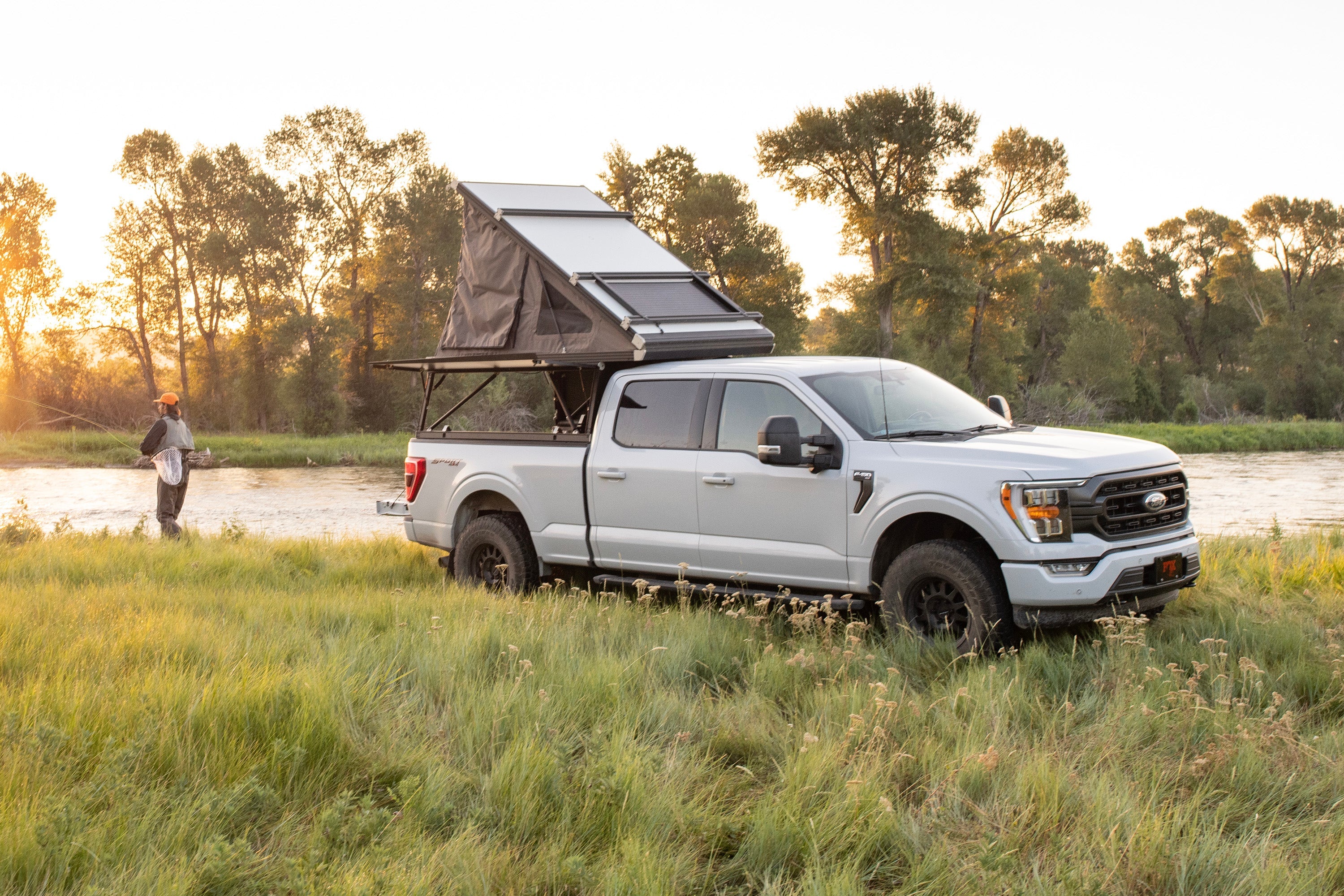 Ford F150 4WD with a 2 inch leveling kit parked by a river, featuring a rooftop tent and a scenic sunset backdrop.