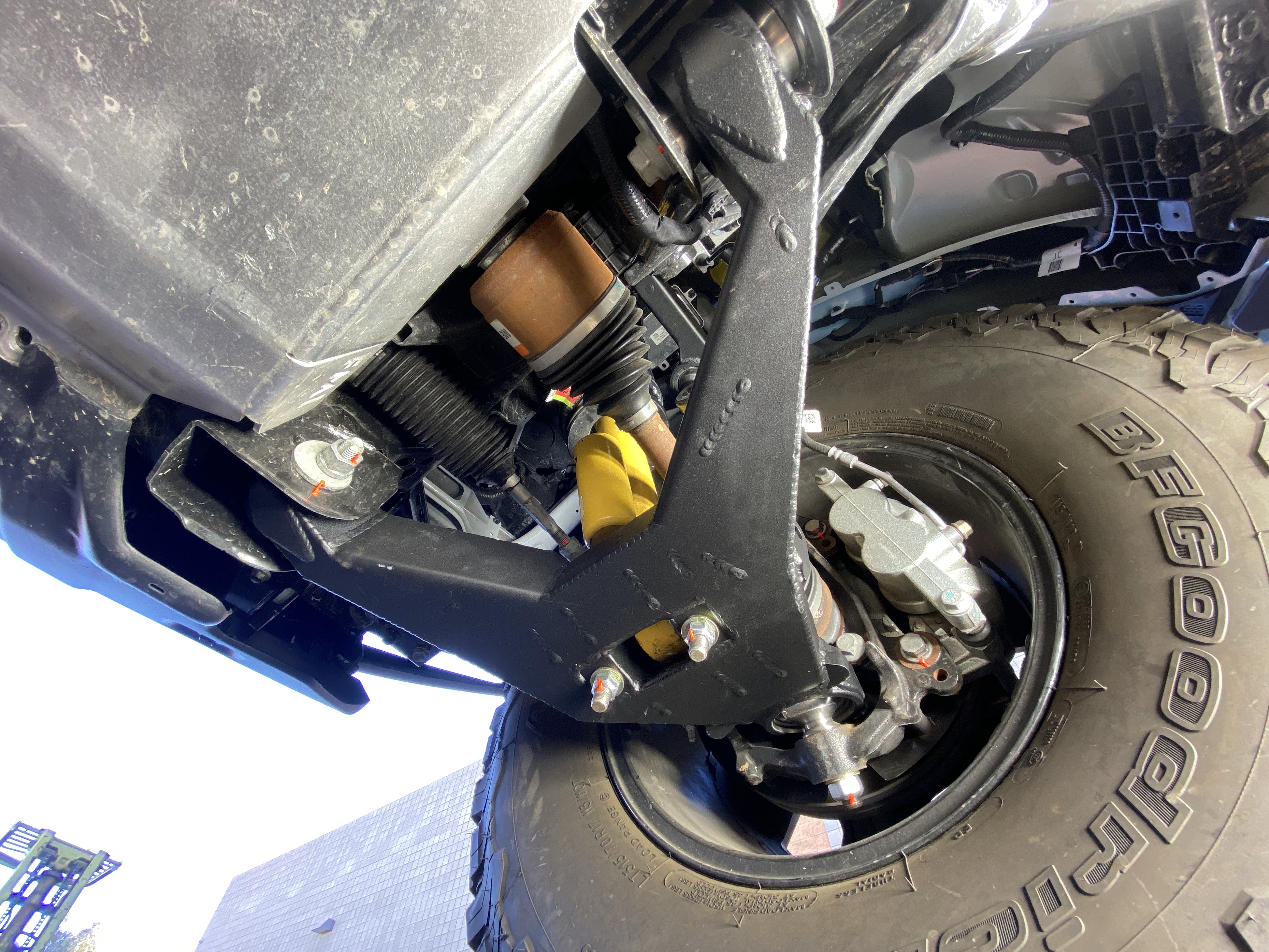 Fabricated lower arm kit for 2021 and newer Bronco, featuring bypass shock mount and stock length, installed on vehicle.