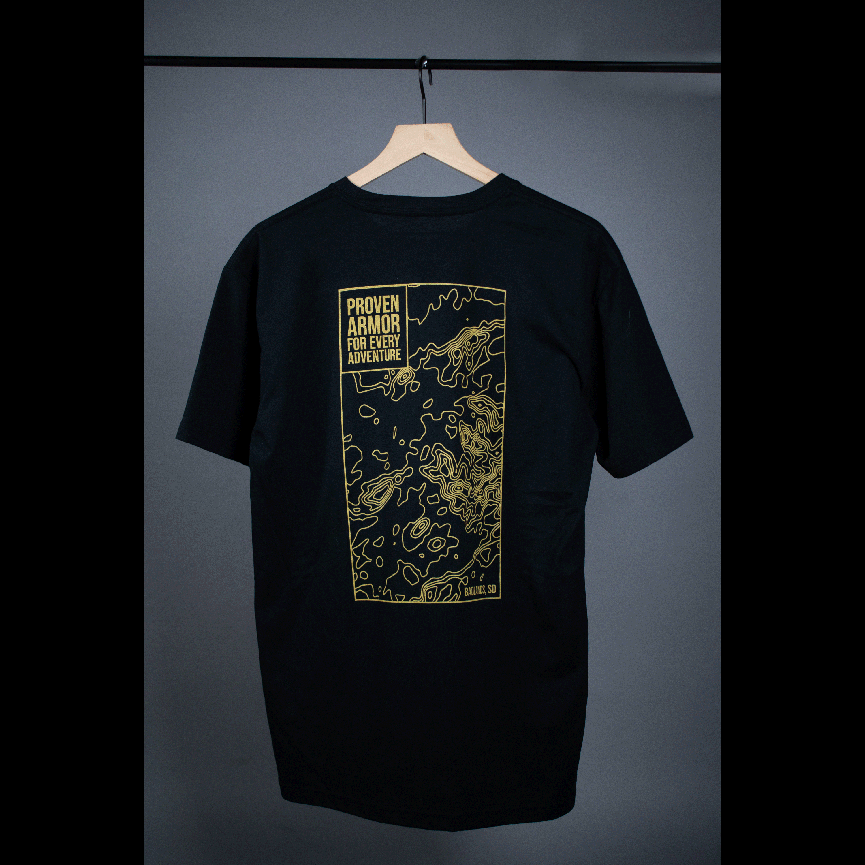 Black Badlands Tee featuring a gold graphic design on the back, highlighting the phrase "Proven Armor for Every Adventure.