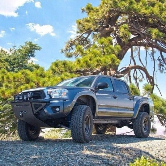 2005-2015 Toyota Tacoma fenders installed on a lifted truck parked in a scenic outdoor setting with trees.