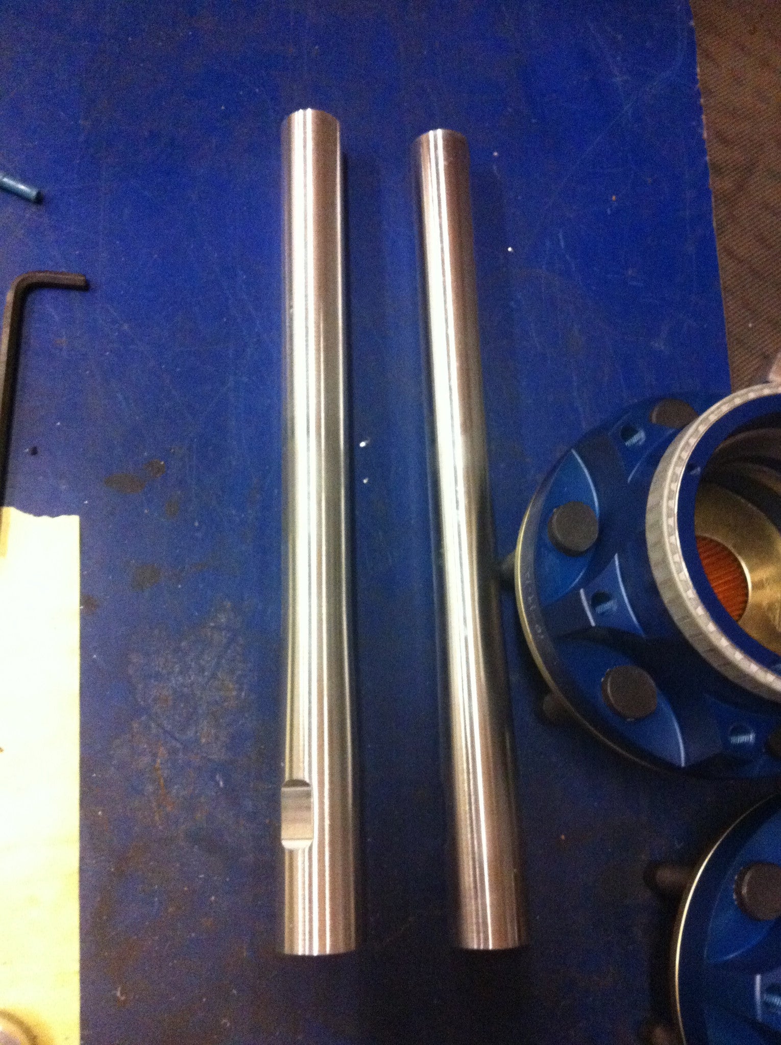 Long travel front suspension kit components for 2010-2014 Raptor, featuring polished metal shafts on a workbench.