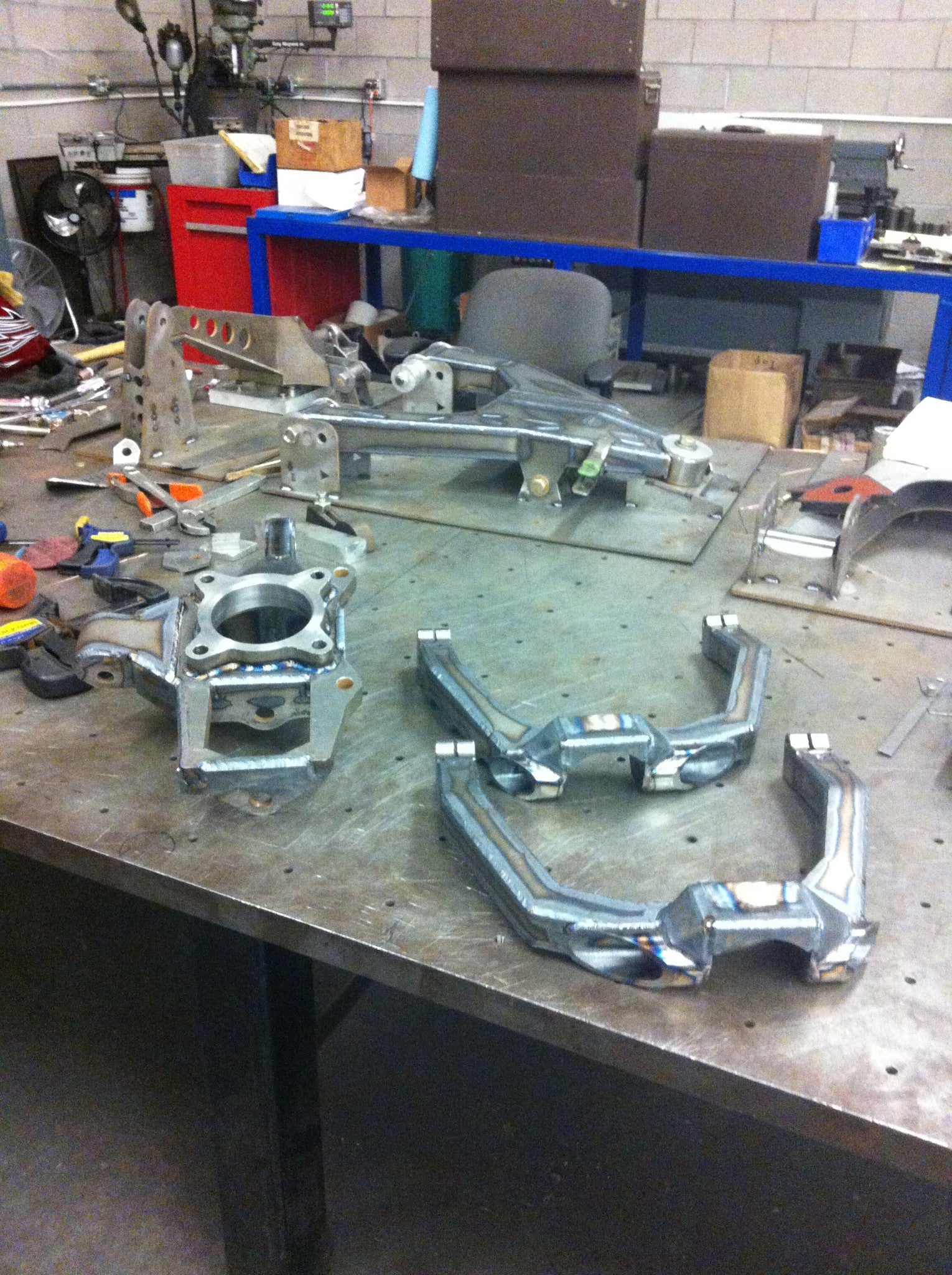 Long travel front suspension kit components for 2010-2014 Raptor, showcasing metal parts on a workshop table.