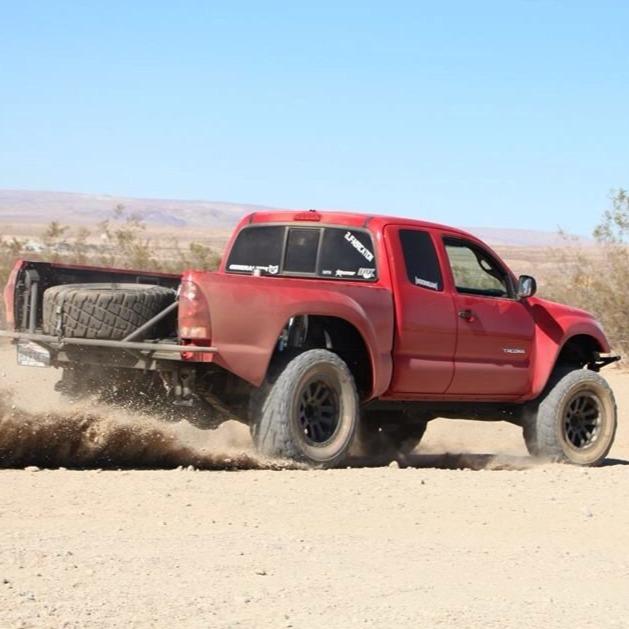 2005-2015 Toyota Tacoma with custom bedsides driving off-road, kicking up dust in a desert landscape.