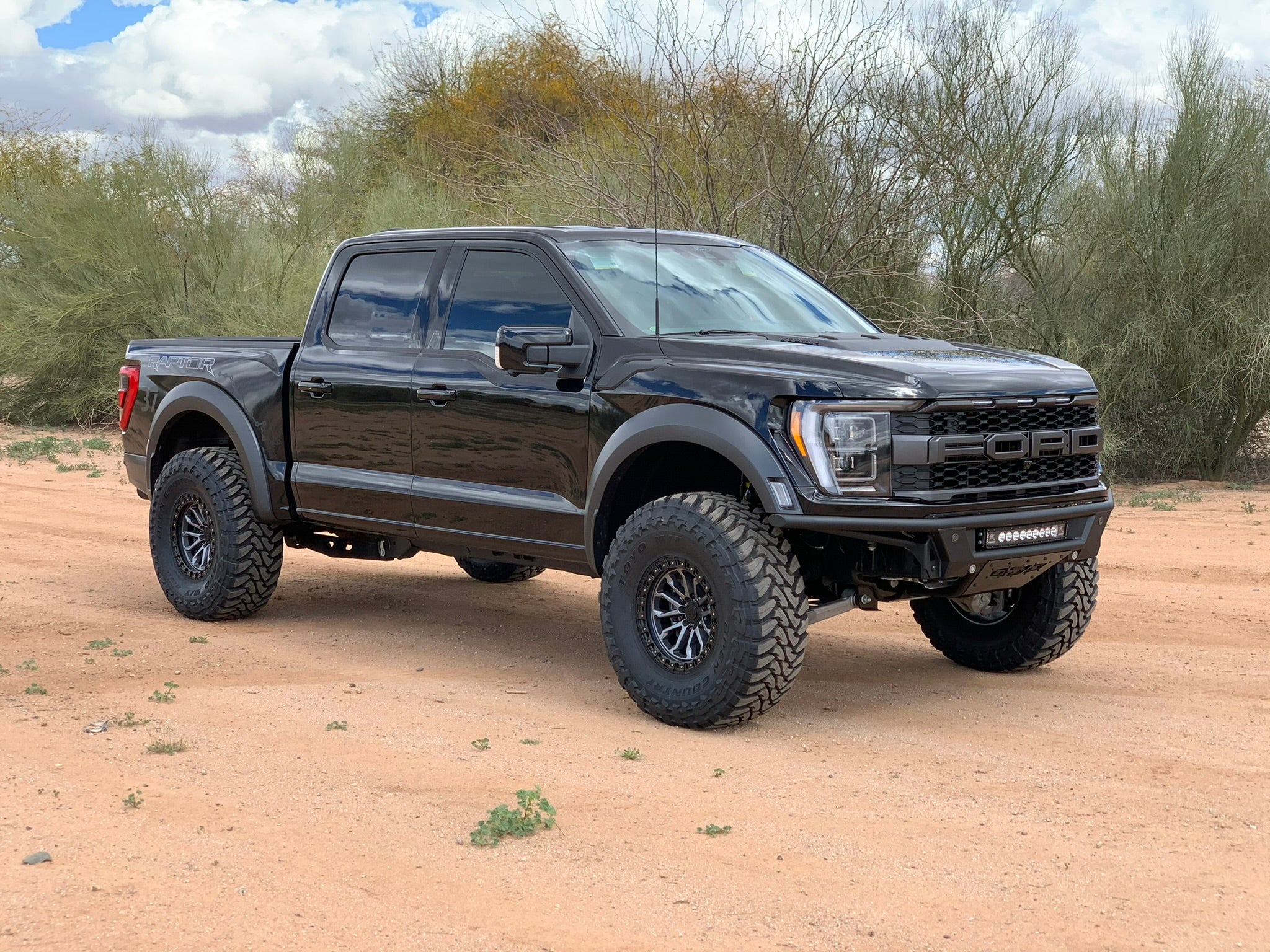 2021 Ford Raptor with a front leveling kit showcasing a 2-inch lift, parked on sandy terrain with desert vegetation.