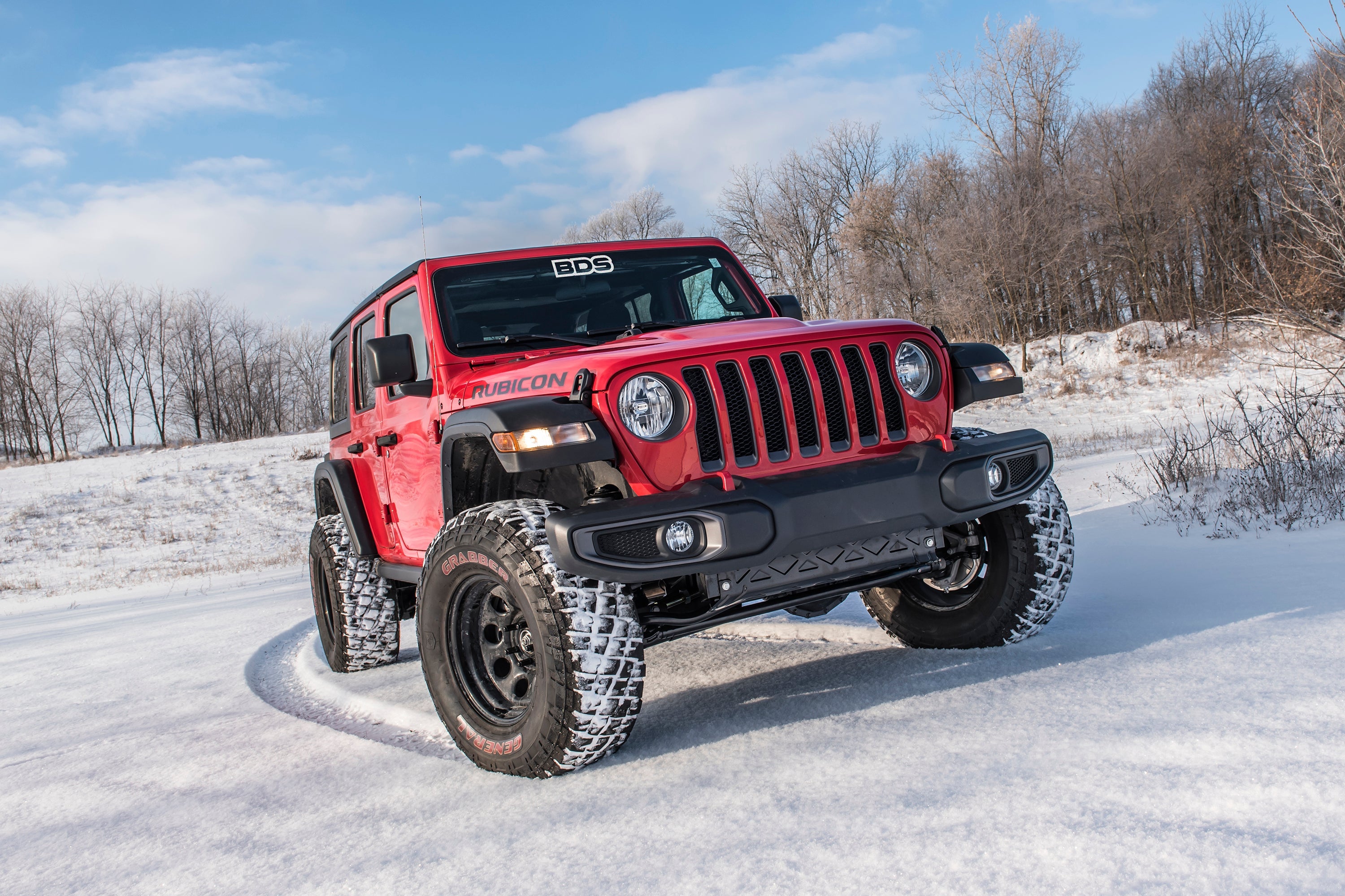 Red Jeep Wrangler JL with a 2-inch lift kit, showcasing enhanced off-road capability in a snowy landscape.