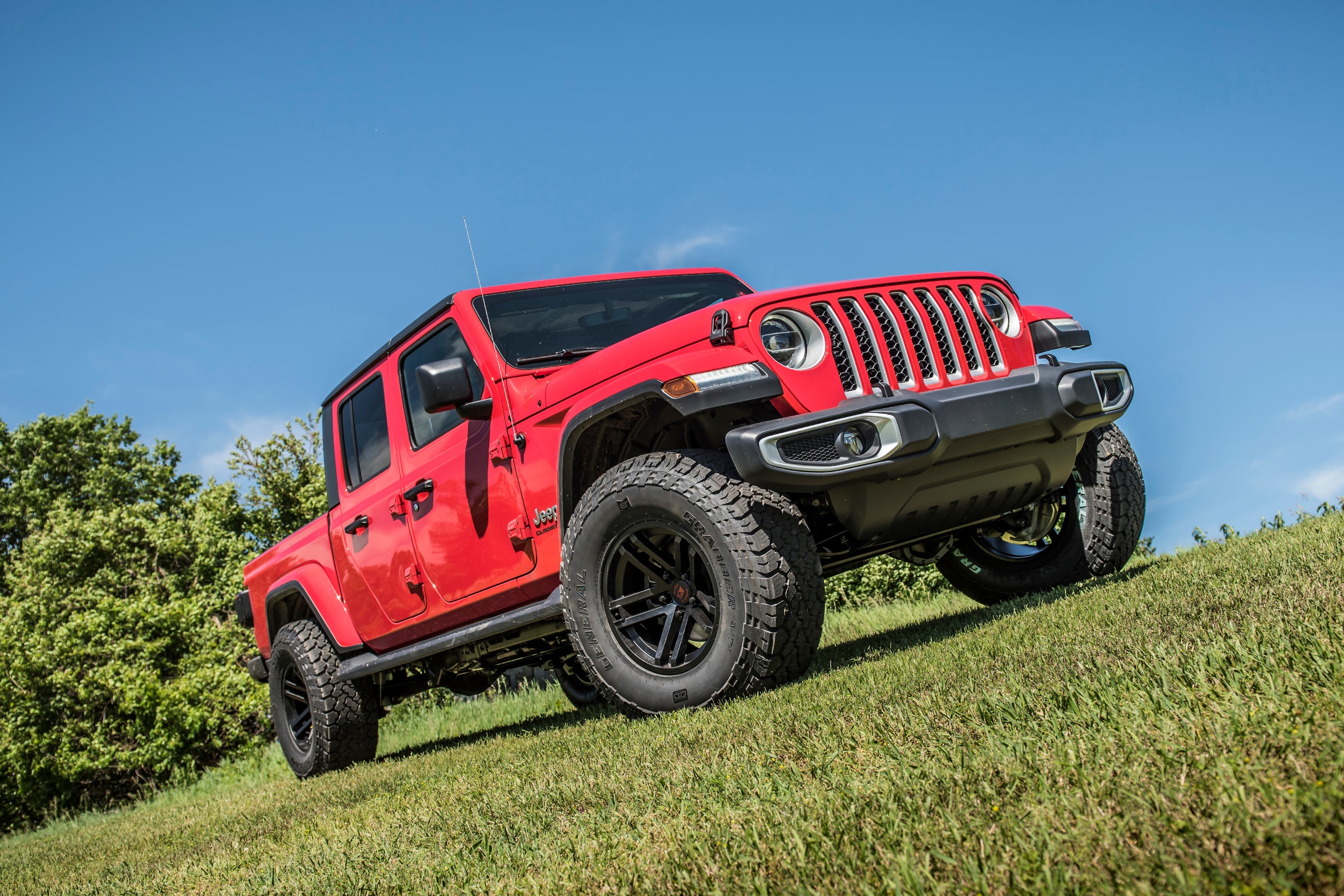 Red Jeep Gladiator JT with a 2-inch leveling kit, showcasing enhanced stance and off-road capability on grassy terrain.