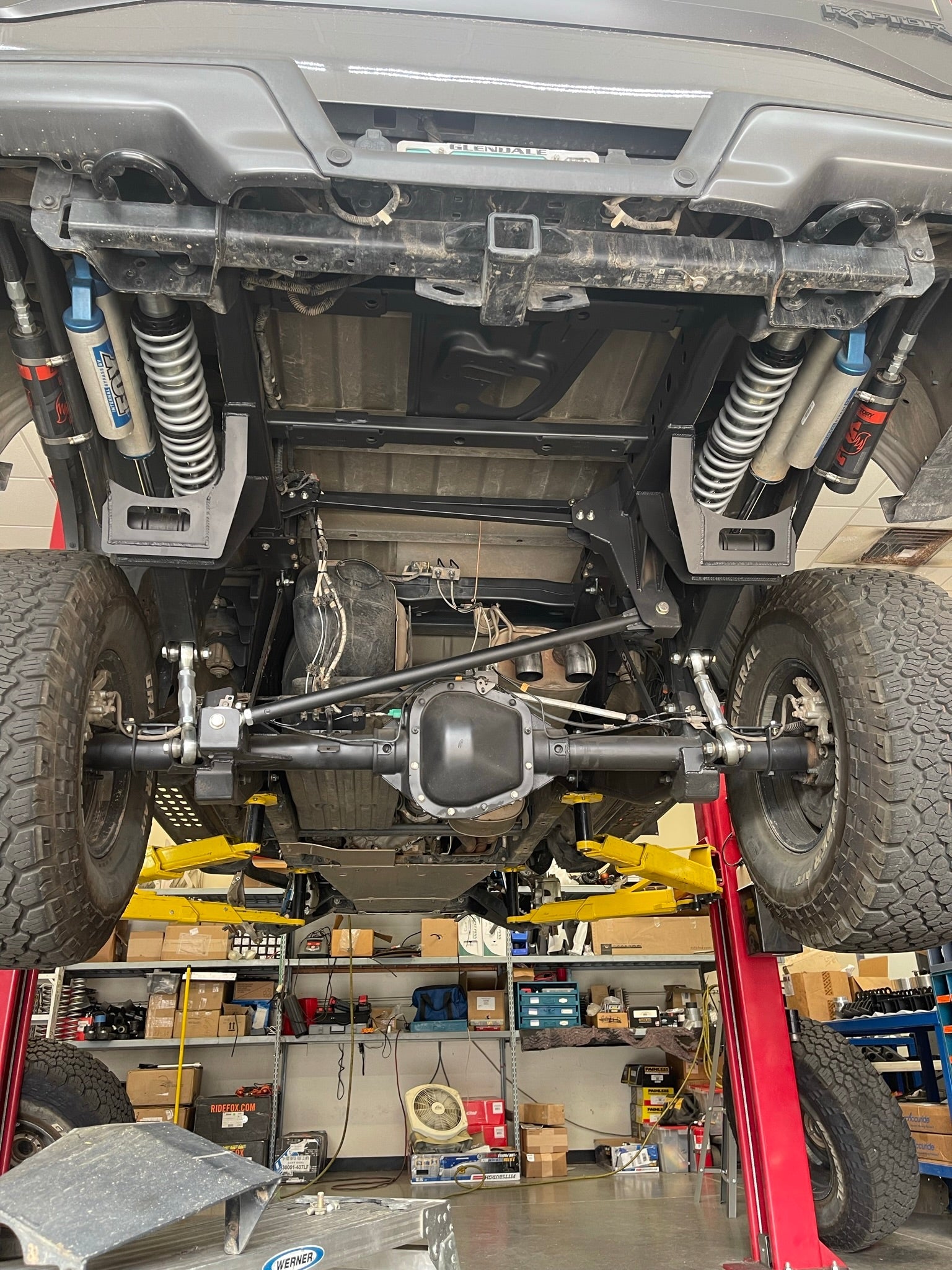 2021-2024 Raptor long travel rear suspension kit showcasing 19 inches of travel, installed on a lifted vehicle in a workshop.