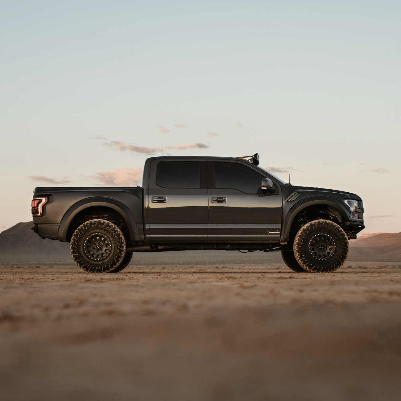 2017-2020 Ford Raptor with custom bedsides, showcasing an aggressive off-road stance in a desert landscape.
