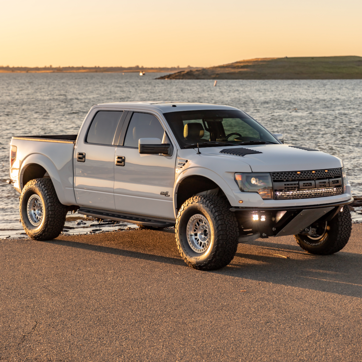2010-2016 Ford Raptor fenders showcased on a silver truck parked by the water, highlighting offroad capabilities.