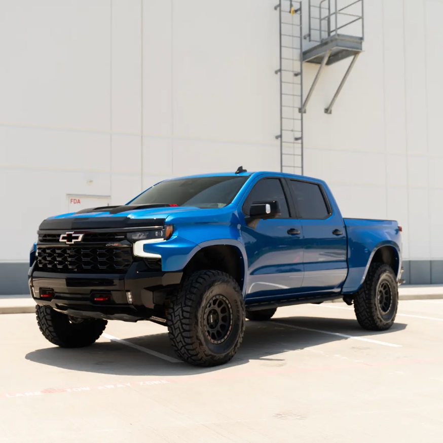Blue 2019-2025 Chevrolet Silverado with aftermarket fenders parked in a lot, showcasing its rugged offroad design.
