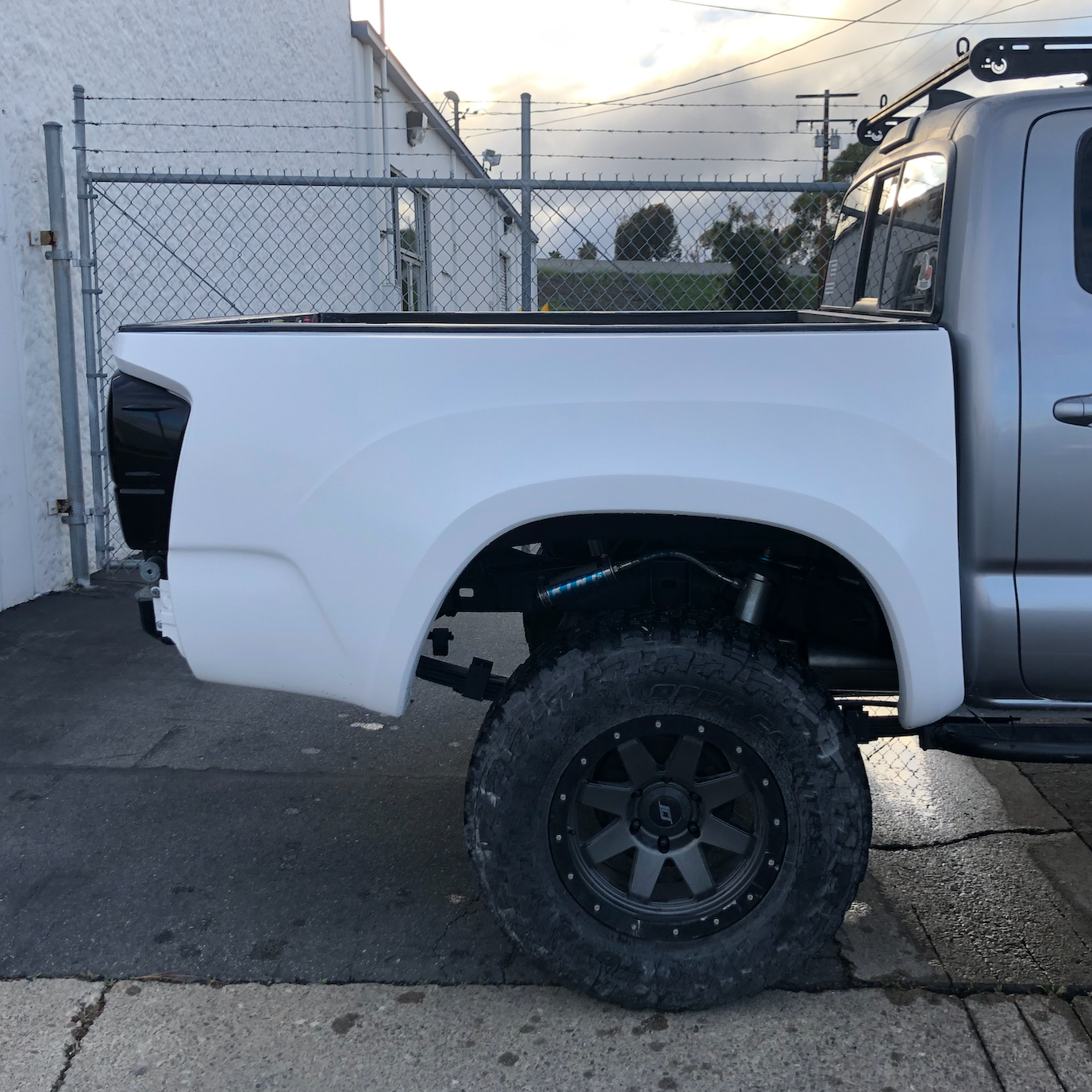 2016-2023 Toyota Tacoma bedsides displayed on a truck with offroad tires, showcasing a sleek white design.