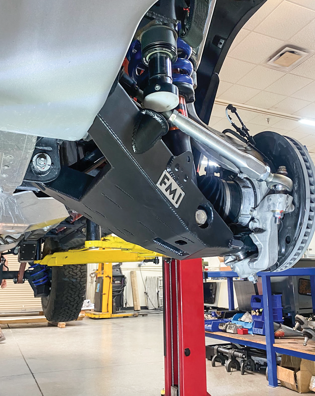 Fabricated lower control arms for 2022+ Bronco Raptor, showcasing stock width and high-performance design in an automotive workshop.
