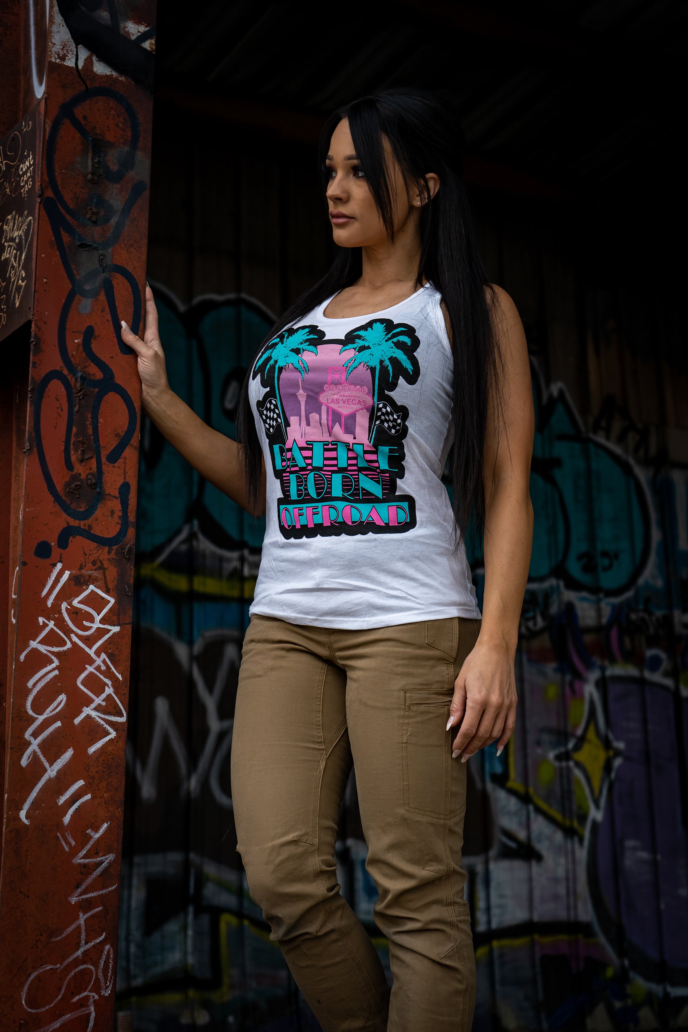 Model wearing a white Miami Vice tank top featuring palm trees and vibrant graphics, standing against a graffiti backdrop.