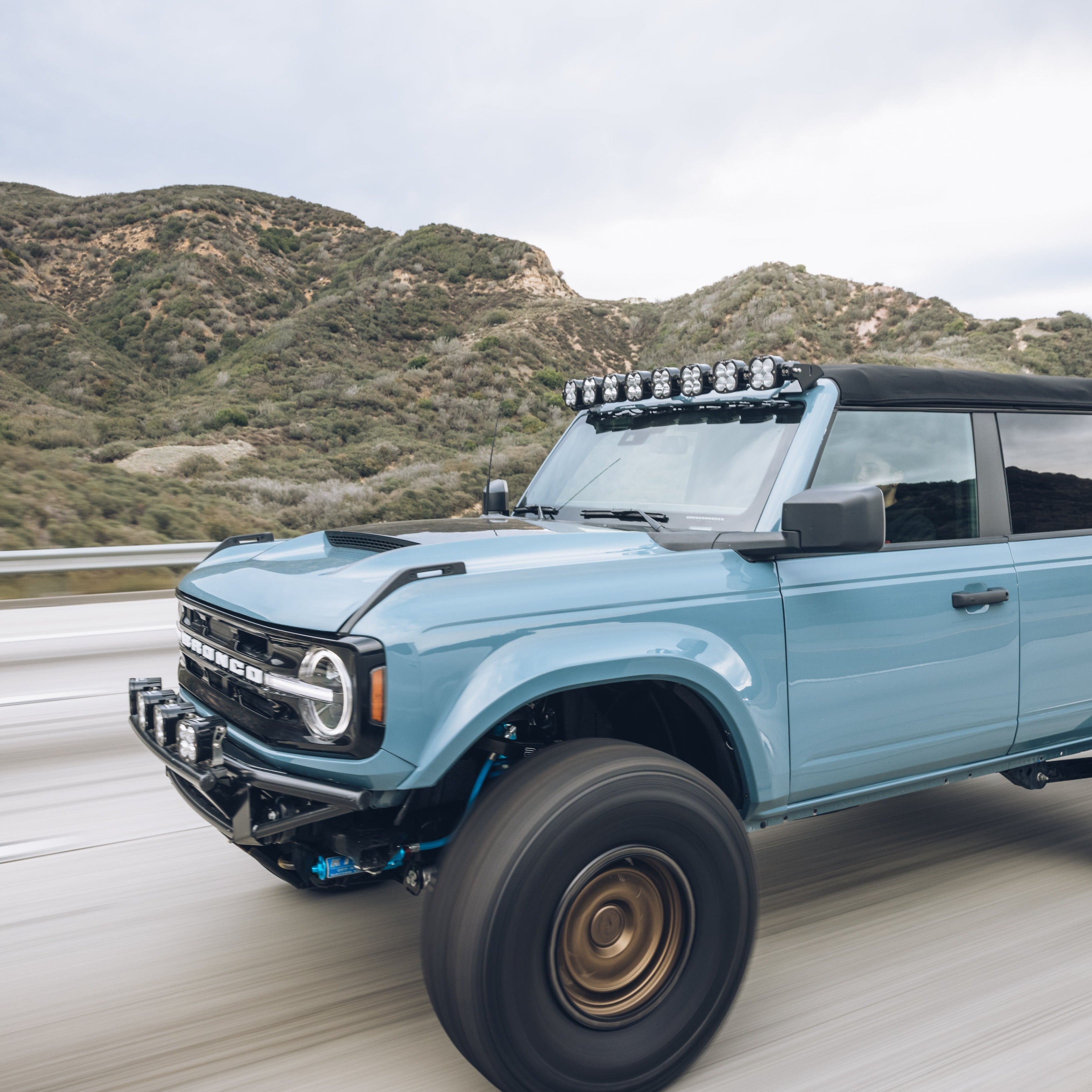 2021-2022 Ford Bronco fenders showcased on a blue Bronco driving on a highway with rugged terrain in the background.
