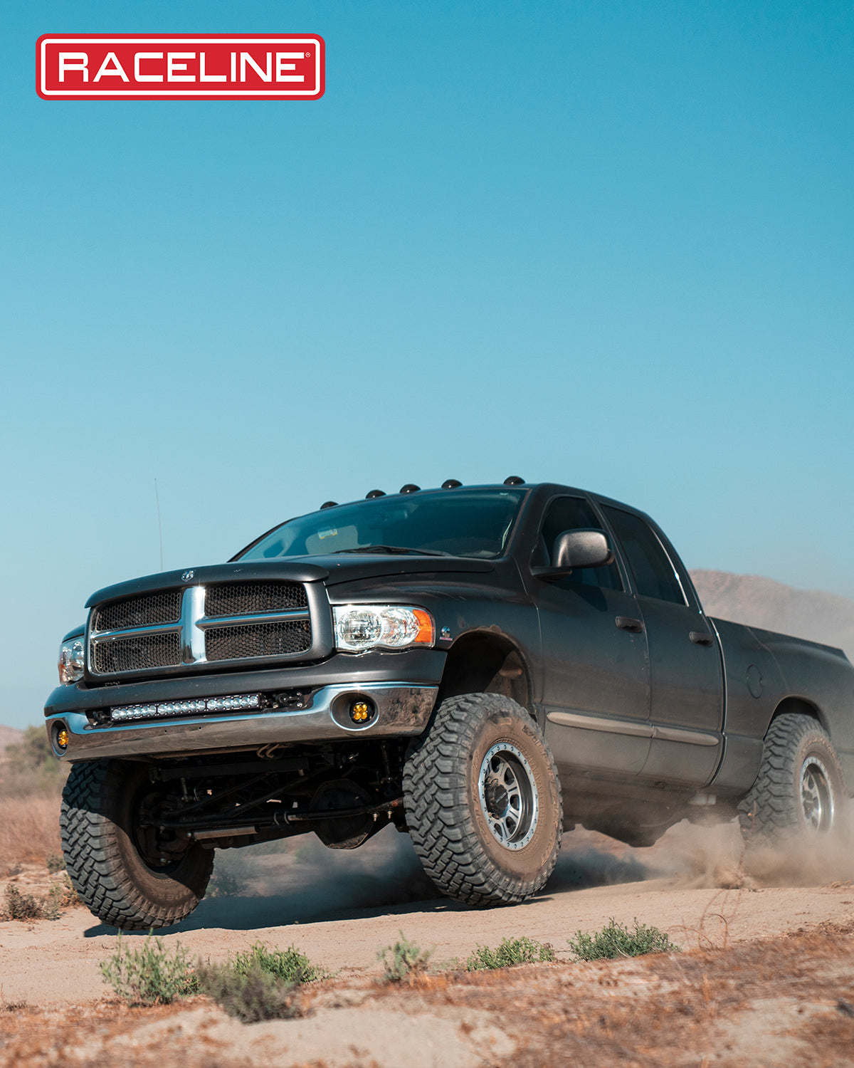Black Dodge truck equipped with Raceline 928M Monster wheels, driving off-road on a dusty trail.