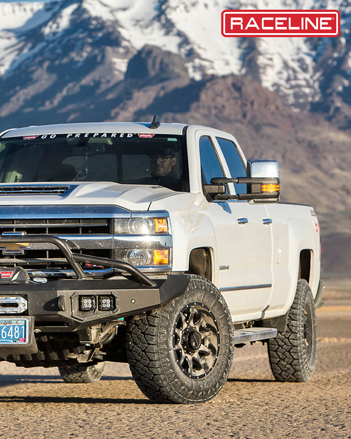 White truck with Raceline wheels and offroad tires parked in a rugged landscape, showcasing its durability and style.