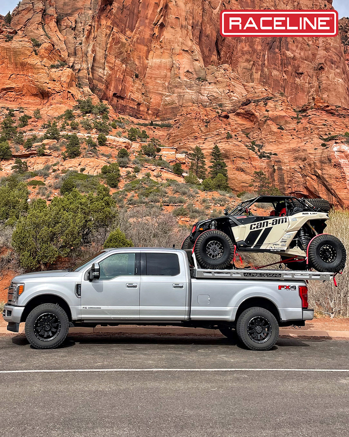 Silver truck with a Can-Am UTV on the bed, parked against a scenic red rock backdrop, showcasing offroad capabilities.