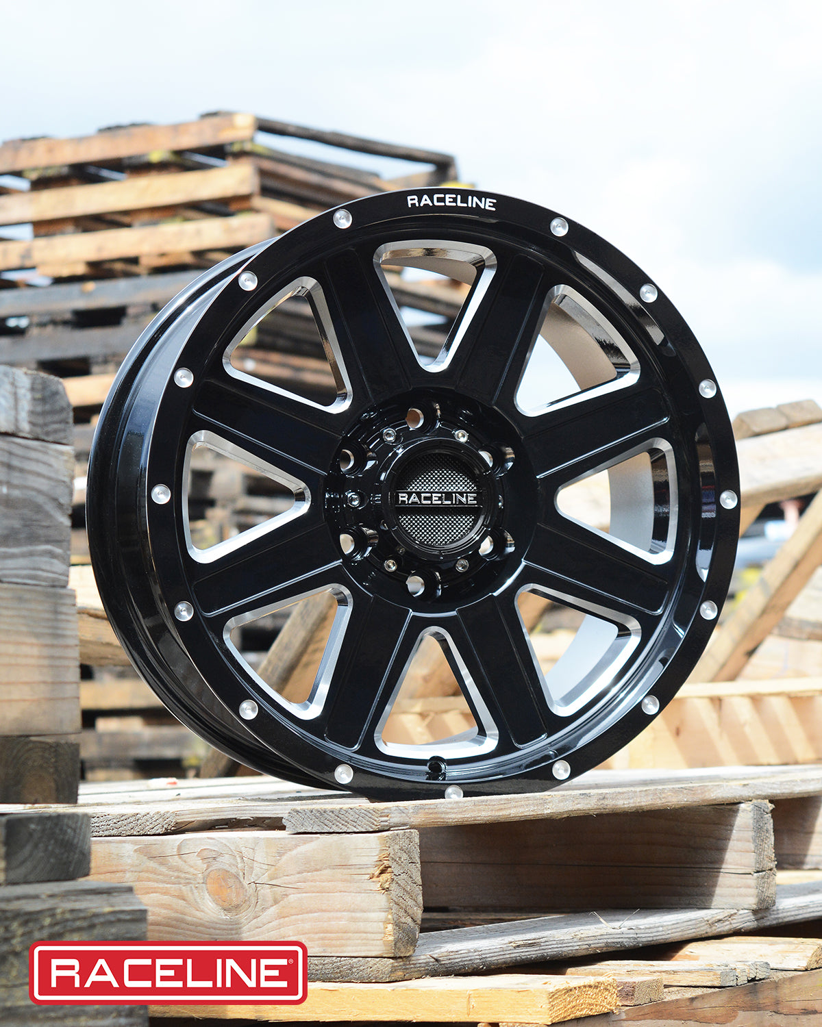 Black Raceline 940M Hostage wheel displayed on wooden pallets, showcasing its sleek design and sturdy construction.