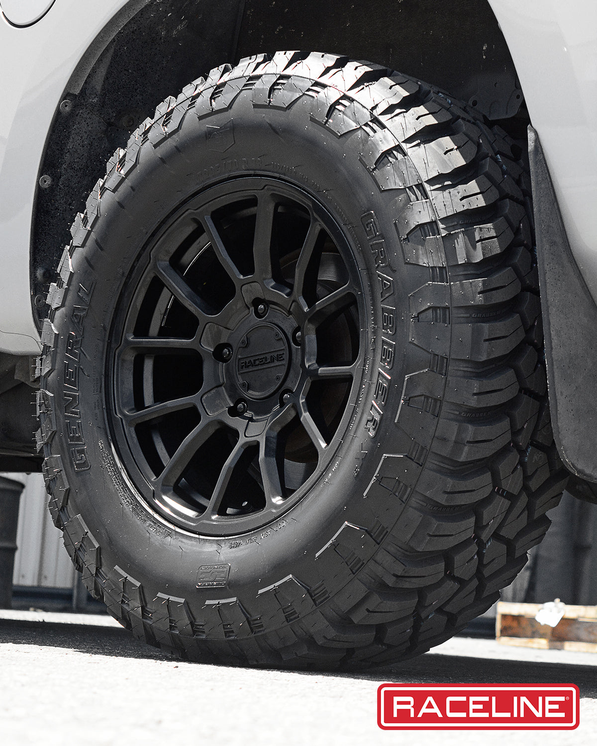 Close-up of a Raceline 950B Gauge wheel mounted on a rugged tire, showcasing a black finish and aggressive tread pattern.