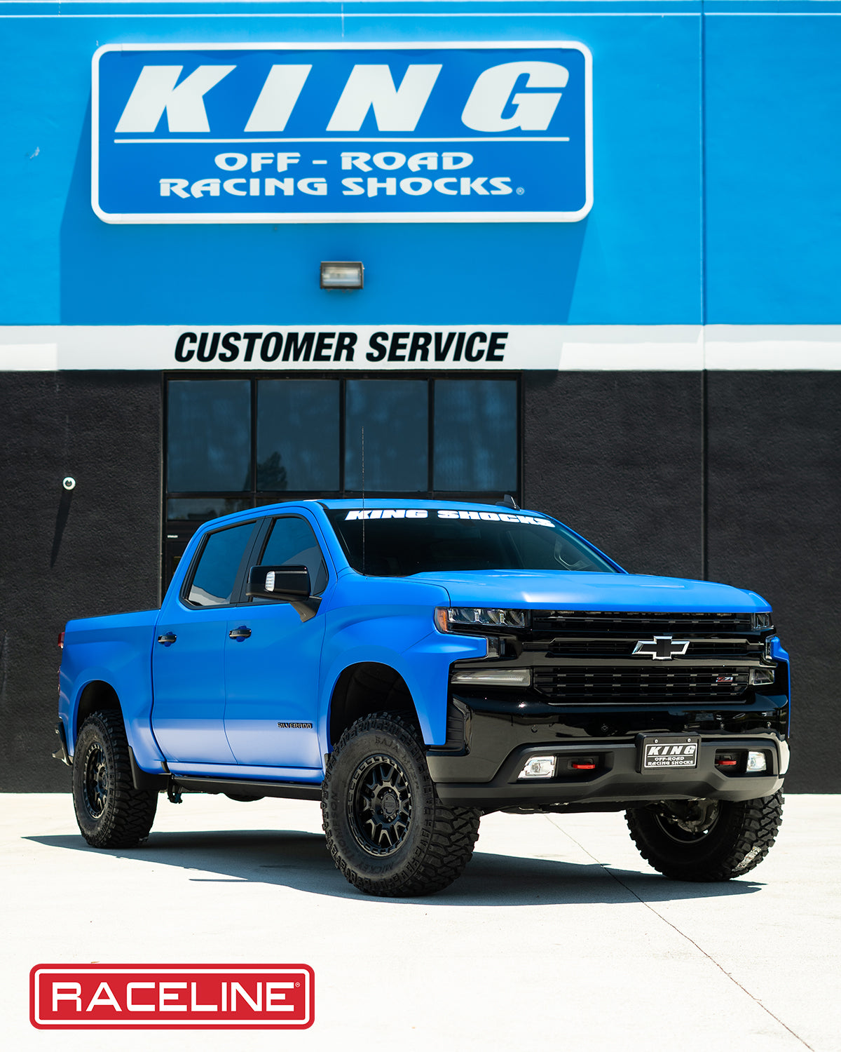 Blue Chevrolet truck equipped with 953B Krank off-road shocks, parked in front of a racing shocks service center.