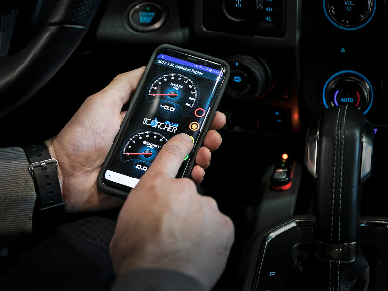 Person using a smartphone to monitor performance metrics for the afe SCORCHER Power Module in a Ford F-150.