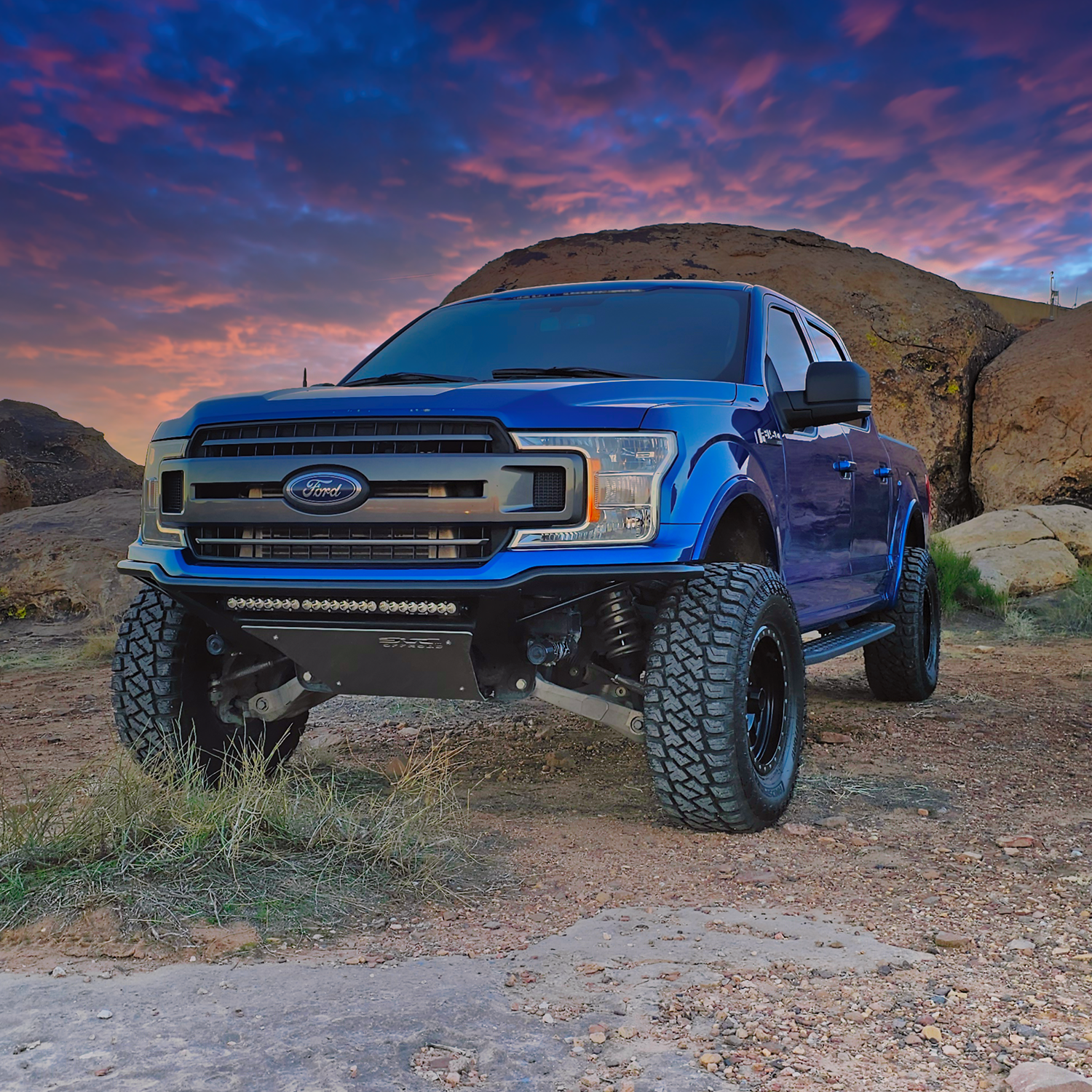 2018-2020 Ford F150 Baja Bumper installed on a blue truck in a rugged outdoor setting with a colorful sky.