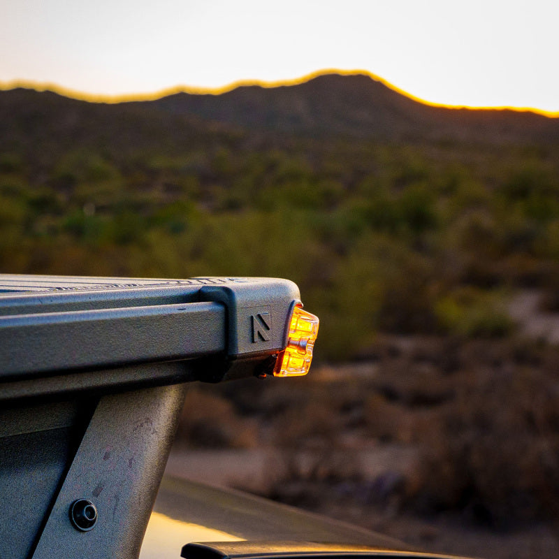 ARB Nacho Nano Base Rack Corner Cap 4-Light Kit installed on a vehicle, showcasing an illuminated corner light against a desert sunset.