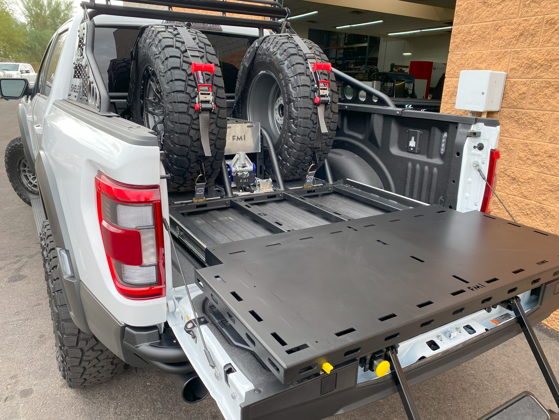 Modular bed organizer for 2017-2024 Ford Raptor with slide-out cargo tray and secured spare tires in truck bed.