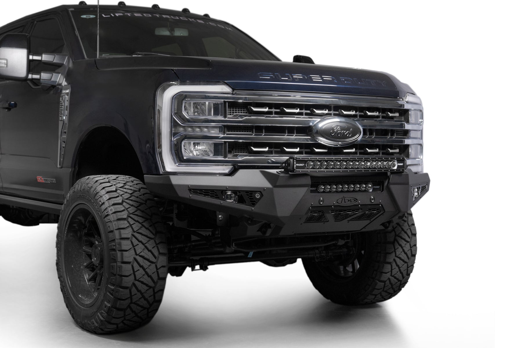 Addictive Desert Designs 2023+ Ford Super Duty Honeybadger Front Bumper on a black truck, showcasing rugged design and offroad capability.