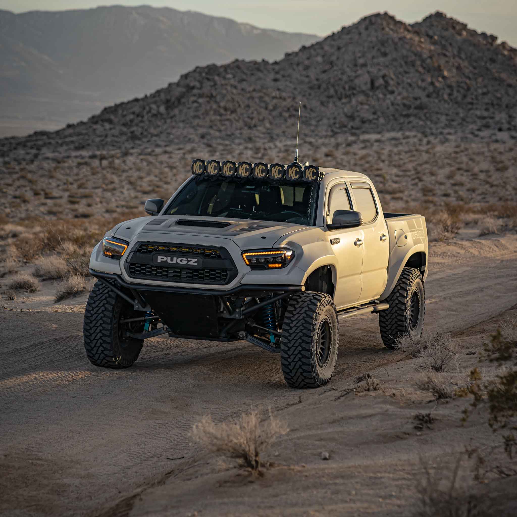2016-2023 Toyota Tacoma fenders on a modified truck driving through a desert landscape with rugged terrain.
