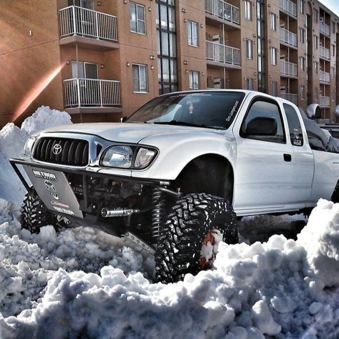 1995-2004 Toyota Tacoma fenders on a lifted white truck navigating through deep snow in an urban setting.