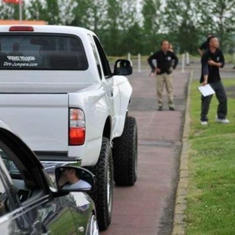 White Toyota Tacoma with aftermarket fenders parked on a road, showcasing its off-road capabilities.