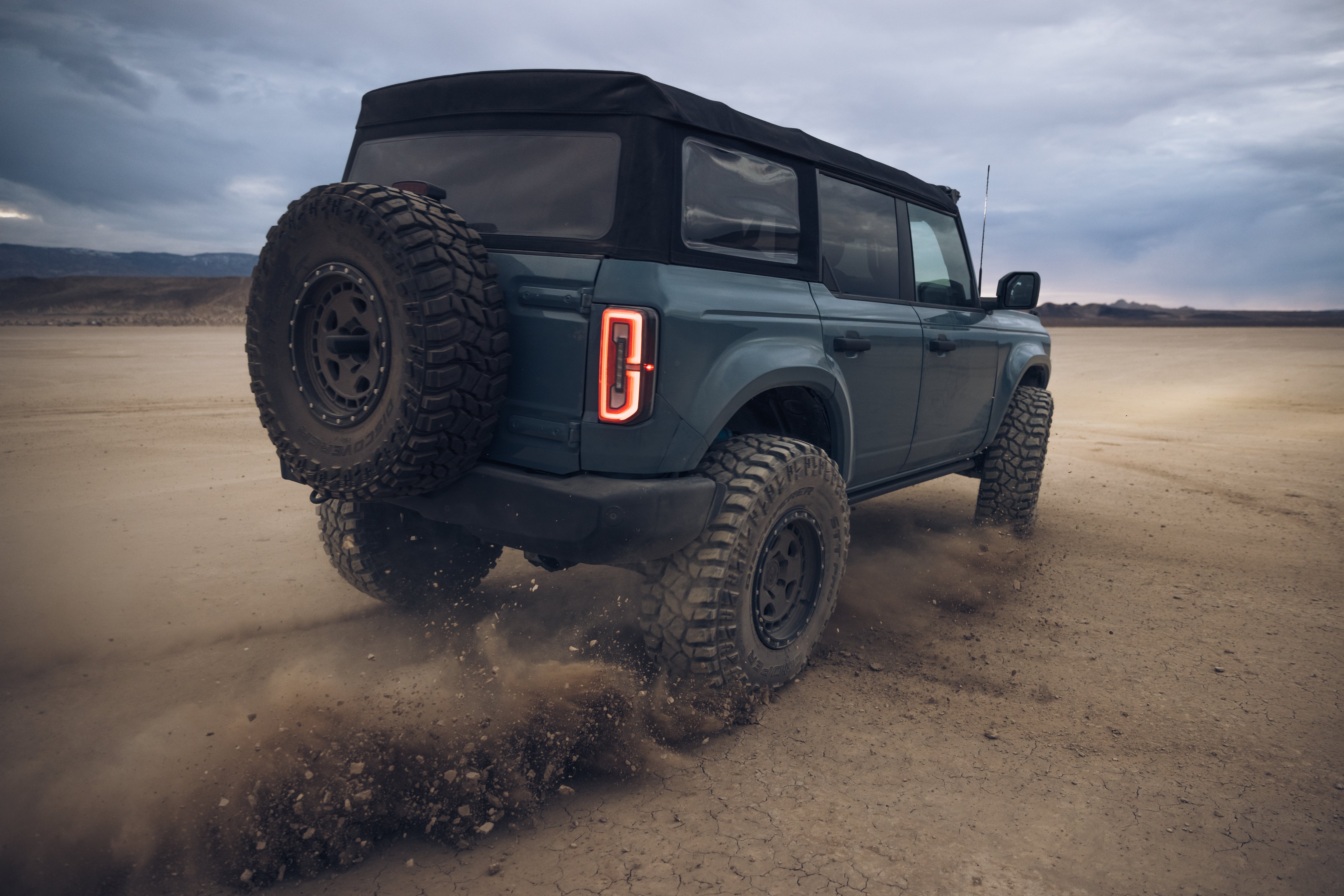 ADV Fiberglass 2021 Ford Bronco with off-road tires kicking up dust in a rugged outdoor setting.