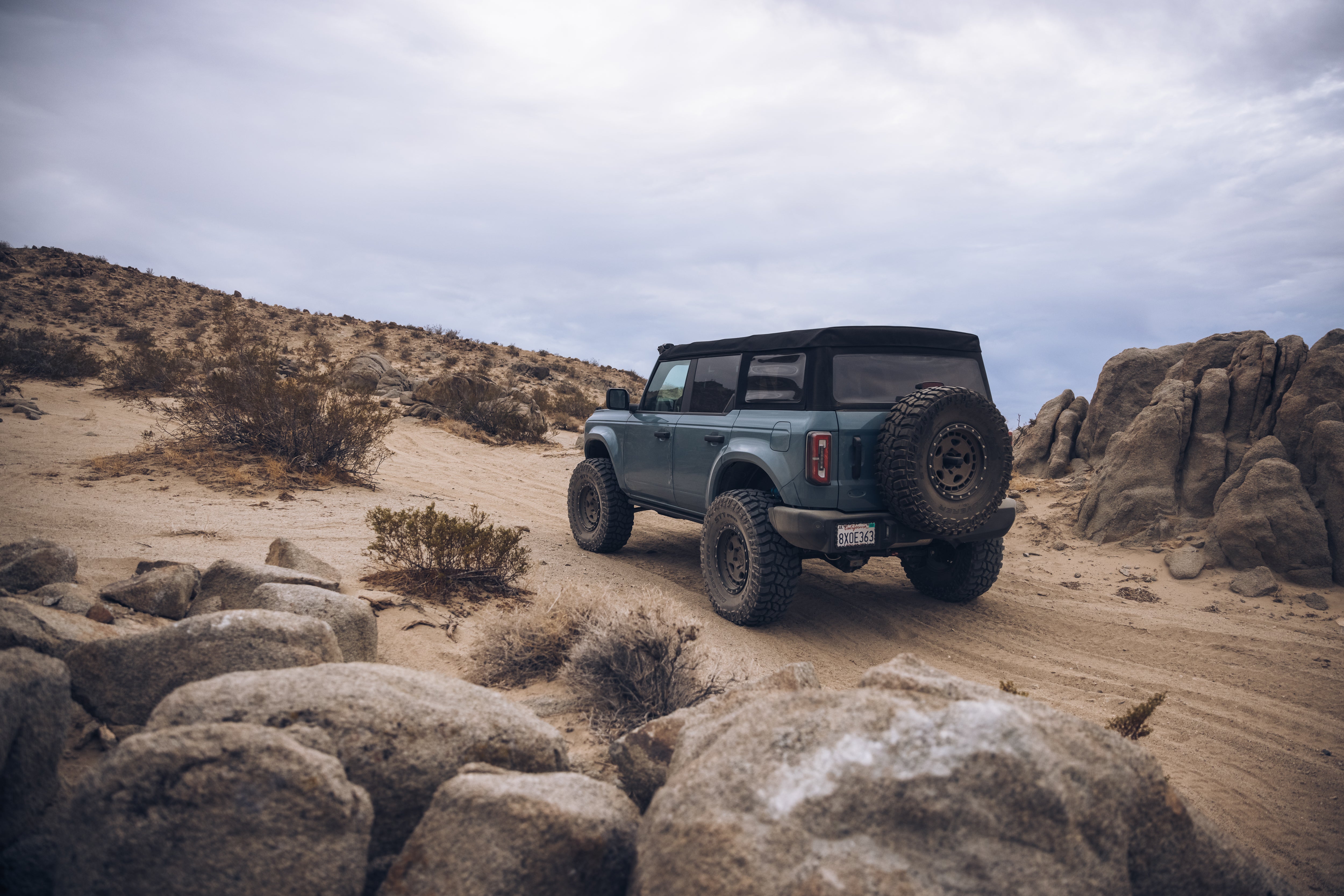ADV Fiberglass 2021 Ford off-road vehicle navigating a rugged desert terrain with rocky formations and sandy trails.