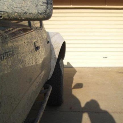 1995-2004 Toyota Tacoma with muddy bedsides parked in front of a garage, showcasing offroad capability and rugged design.