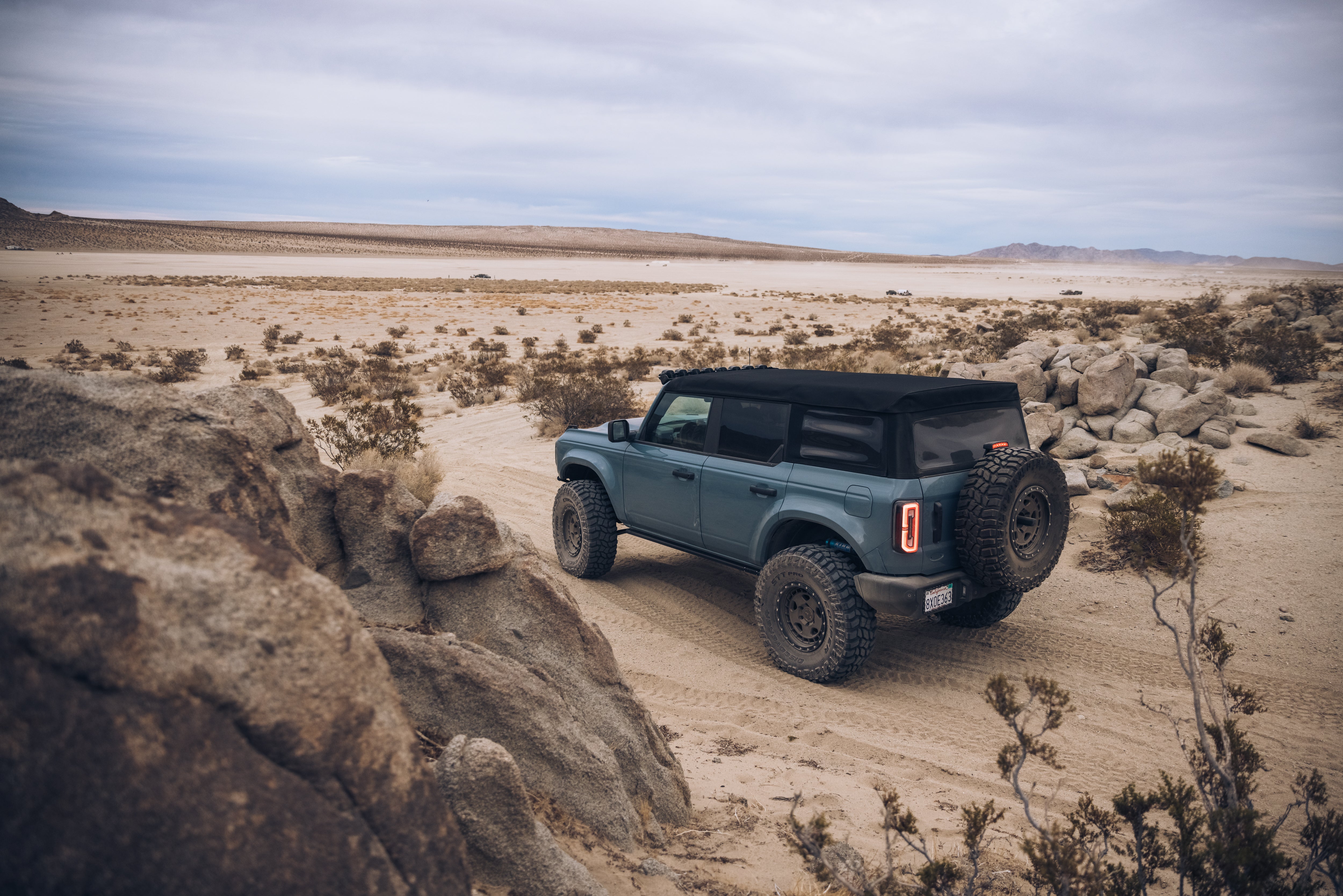 ADV Fiberglass 2021 Ford Bronco parked on sandy terrain, showcasing rugged tires and a soft top in an offroad setting.