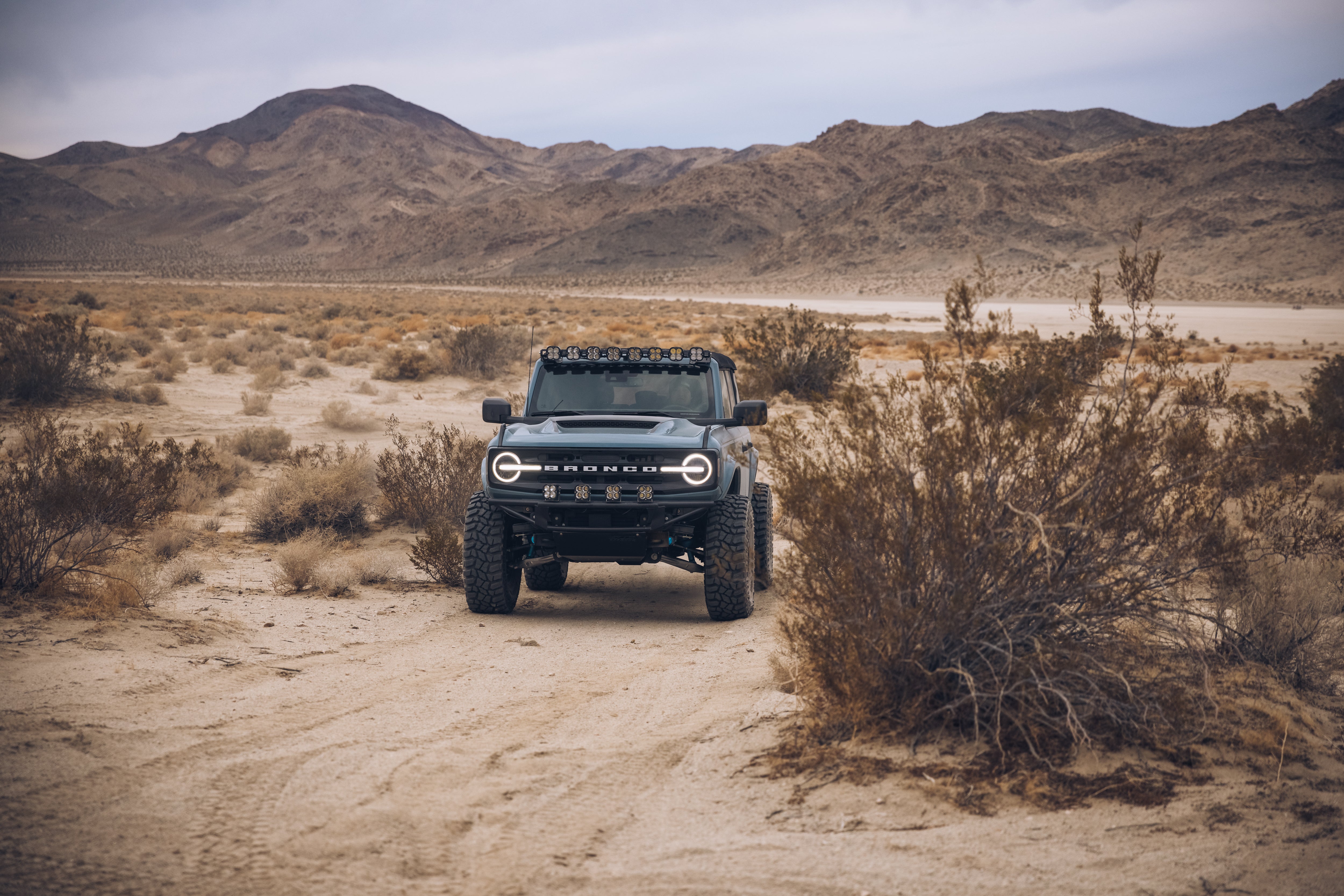 ADV Fiberglass 2021 Ford Bronco in a desert landscape, showcasing off-road capabilities with rugged terrain and mountains in the background.
