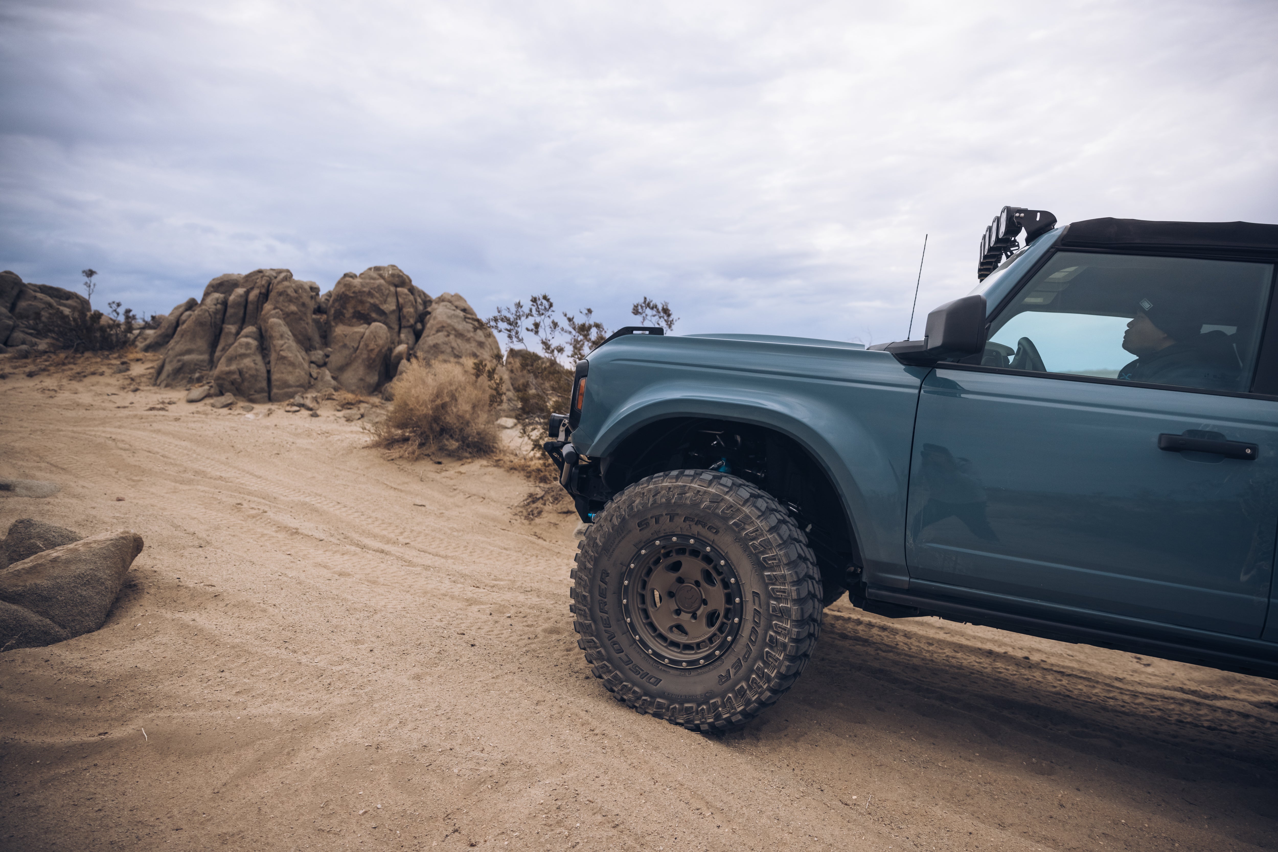 ADV Fiberglass 2021 Ford truck navigating a rugged off-road terrain with rocky formations in the background.