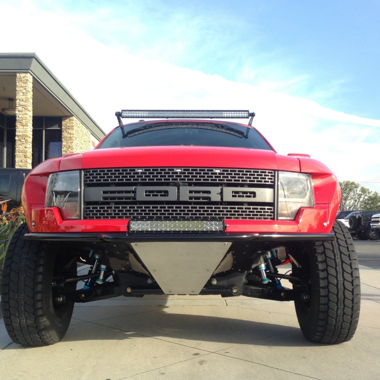 Front view of a red 2010-2016 Ford Raptor showcasing aftermarket fenders and rugged off-road tires.