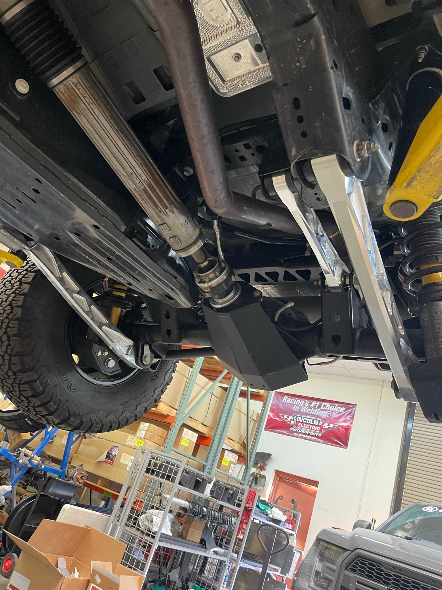 Bronco rear suspension kit featuring billet aluminum rear arms installed under a vehicle in a workshop setting.
