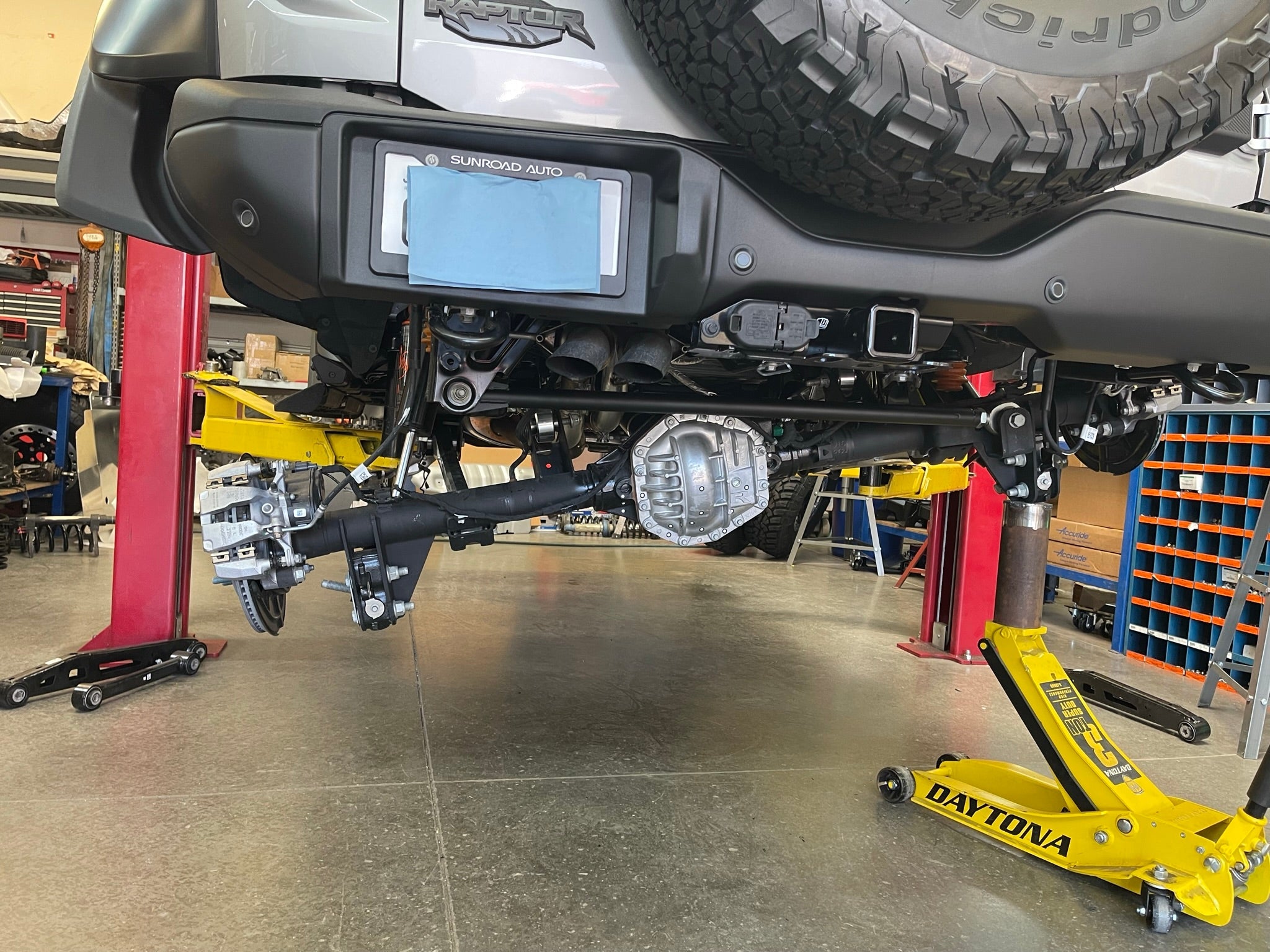 Bronco Raptor rear suspension kit featuring billet aluminum rear arms, installed on a lifted vehicle in a workshop.