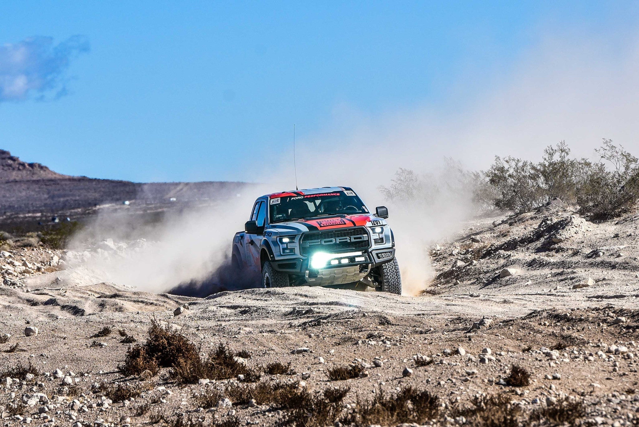 Ford Raptor race truck navigating rough terrain, showcasing the front bumper light bar mount kit in action.