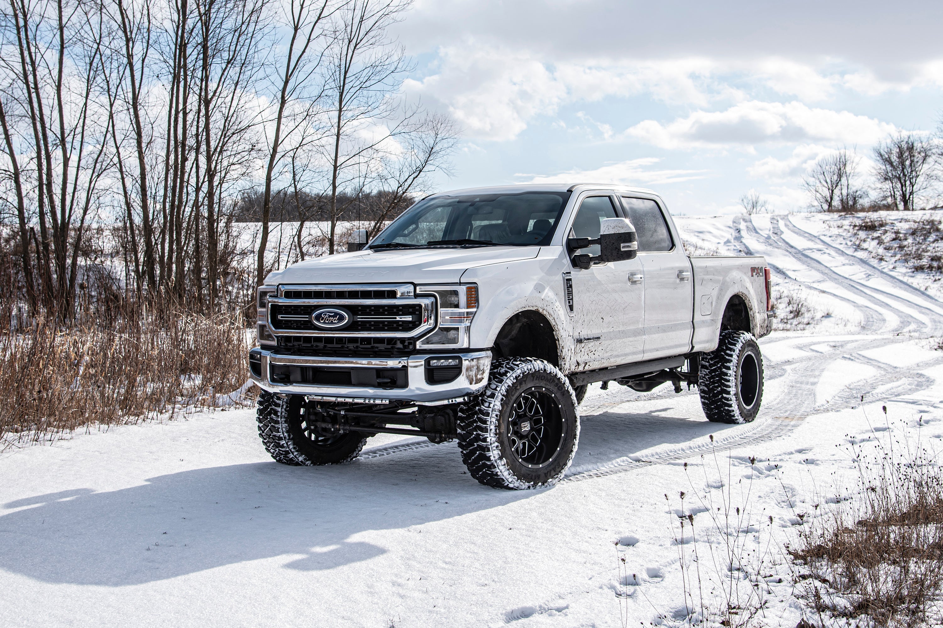 7-inch lift kit with 4-link and FOX 2.5 coil-over conversion installed on a Ford F250 Super Duty in snowy terrain.