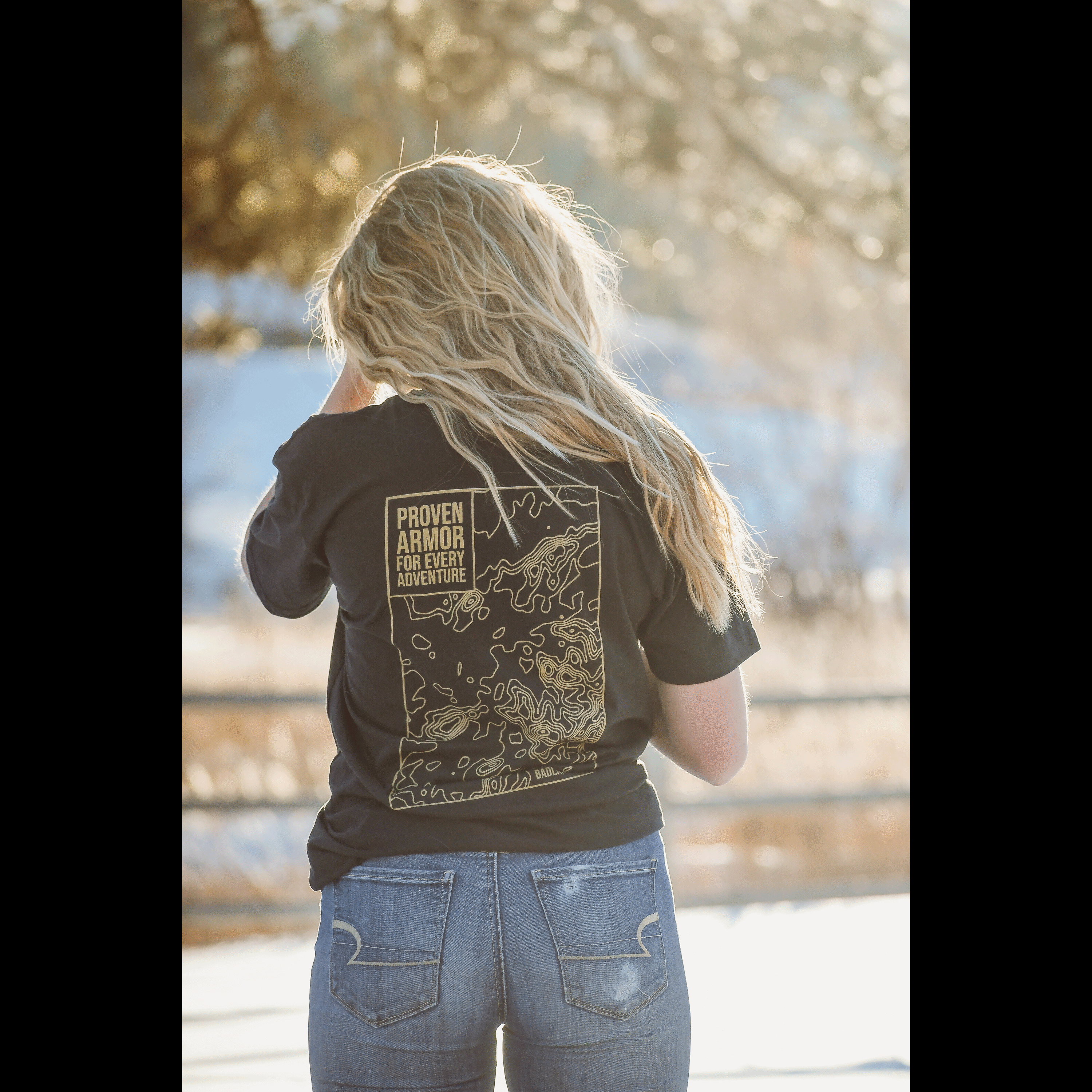 Woman wearing a black Badlands Tee with a graphic design on the back, showcasing outdoor adventure themes.