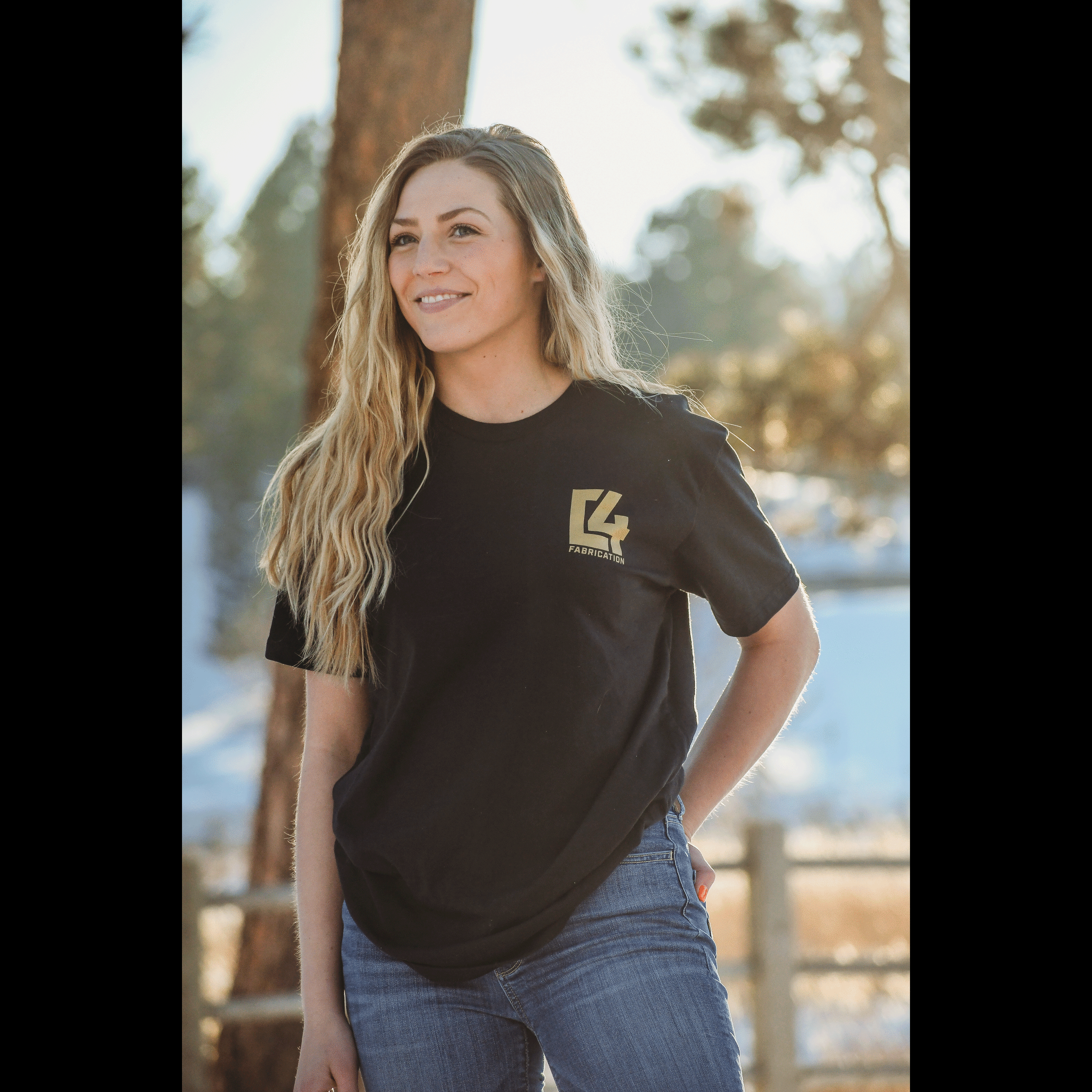 Woman wearing a black Badlands Tee with a gold logo, standing outdoors in a natural setting.