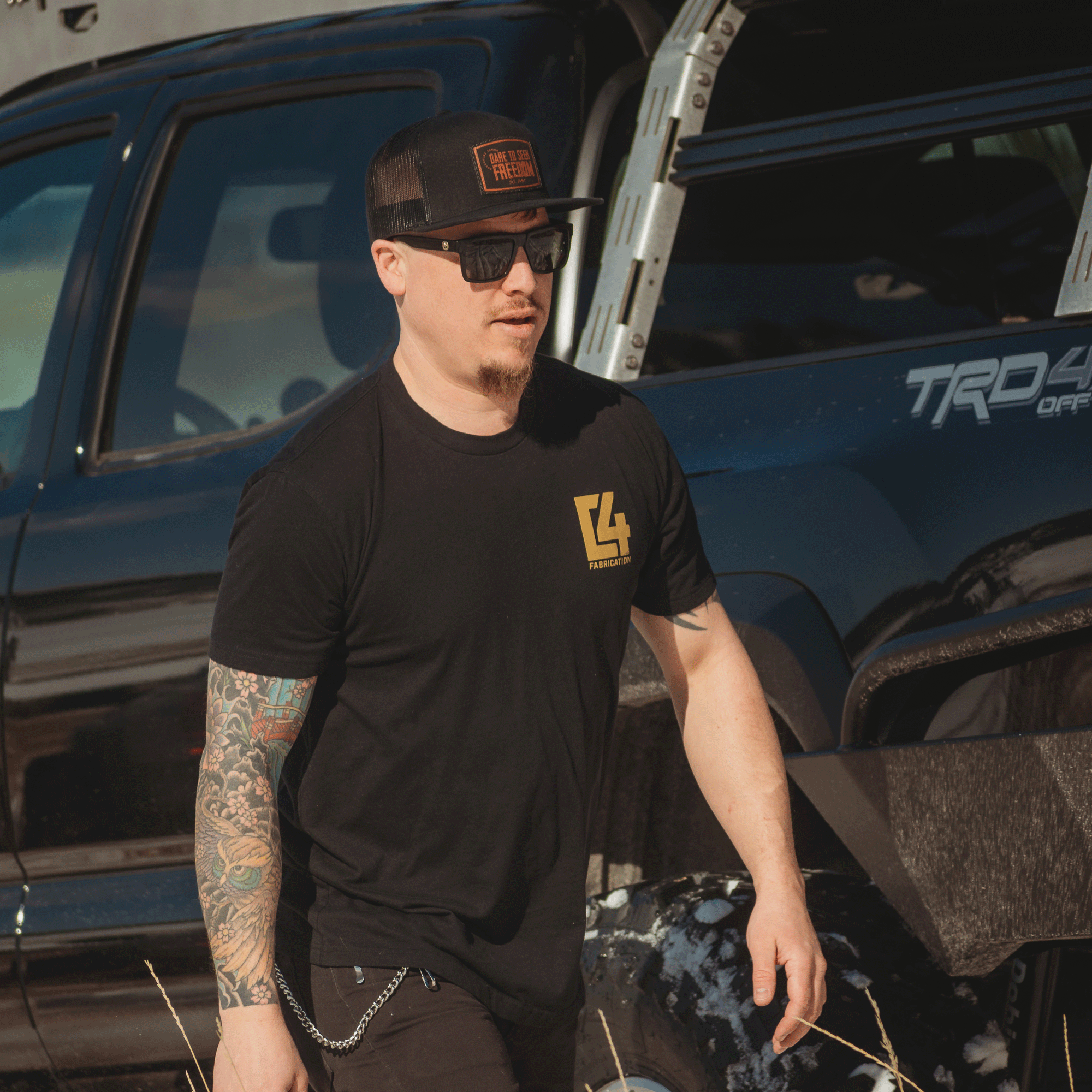 Man wearing a black Badlands Tee with a logo, walking near a truck, showcasing an offroad lifestyle.