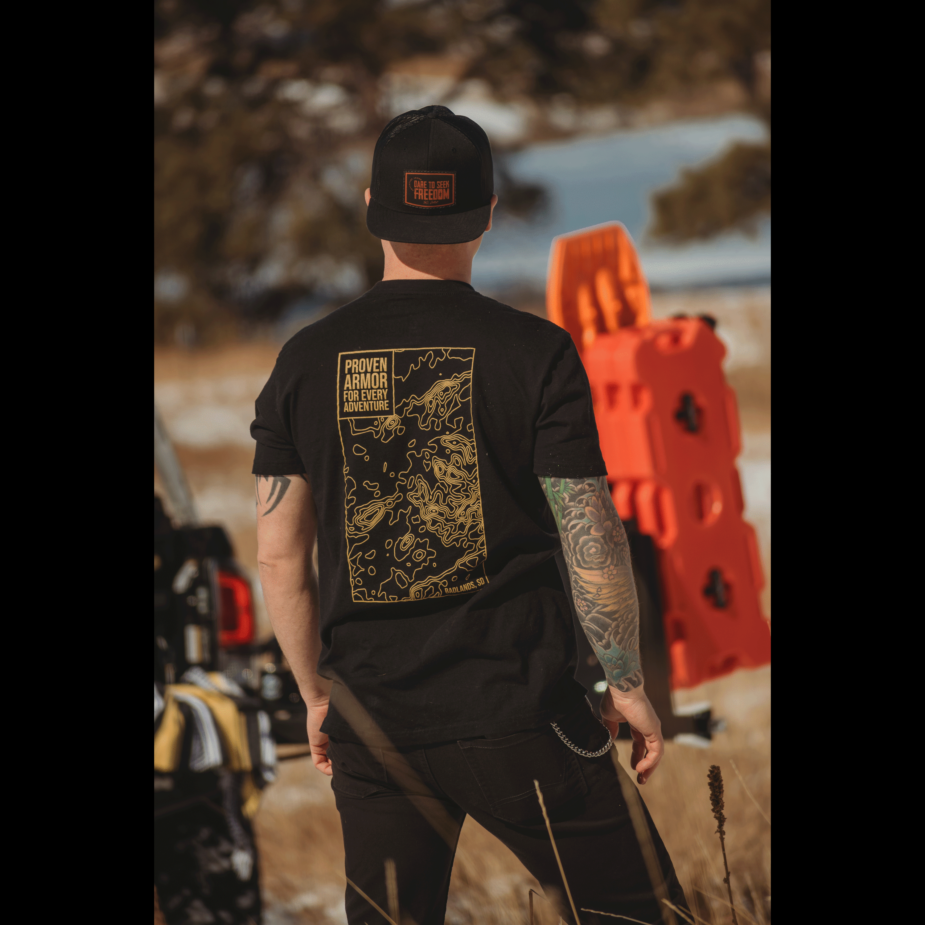 Man wearing a black Badlands Tee with a graphic design on the back, standing in an outdoor setting.